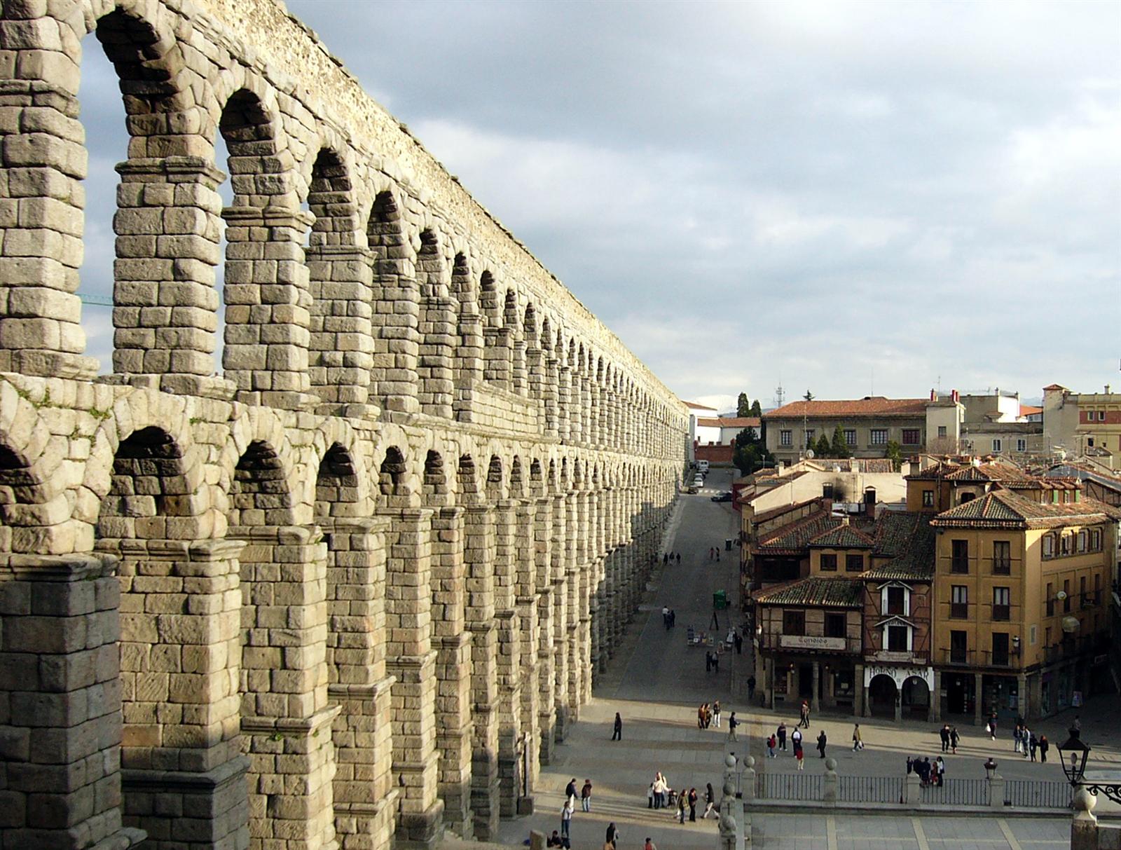 El Acueducto Romano de Segovia fotografiado desde un ángulo bajo, destacando la escala monumental de los dos pisos de arcos de granito sobre la Plaza del Azoguejo