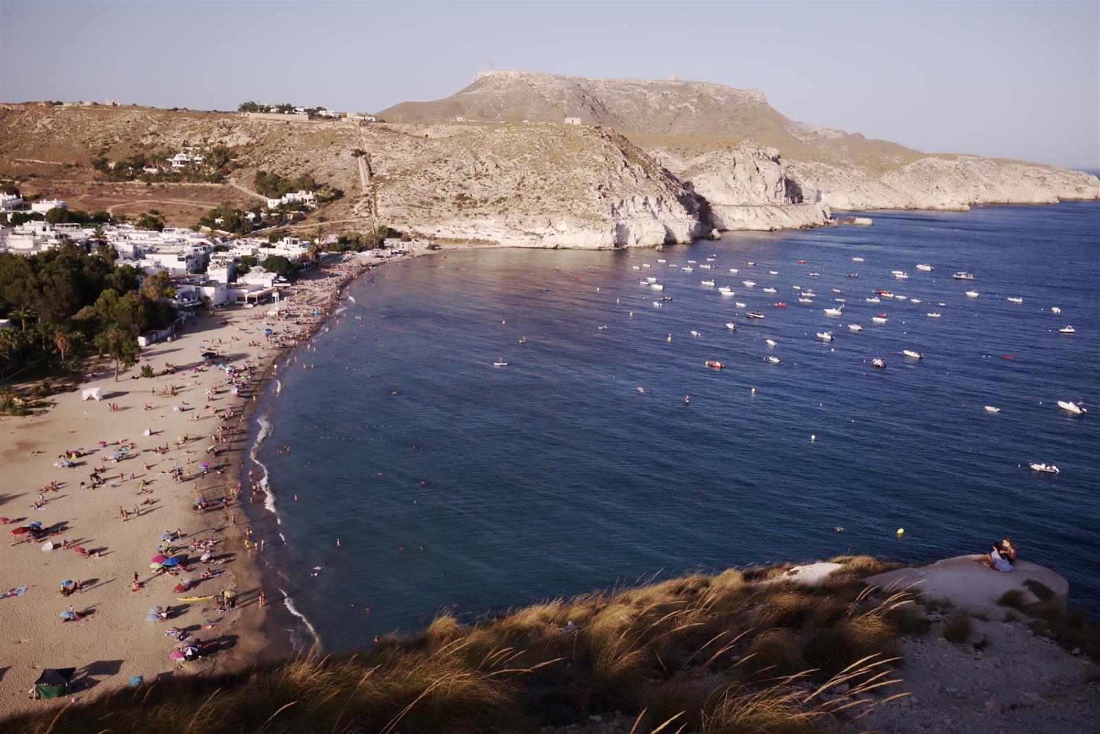 Vista general de la playa de Agua Amarga con el pueblo al fondo y bañistas en la orilla