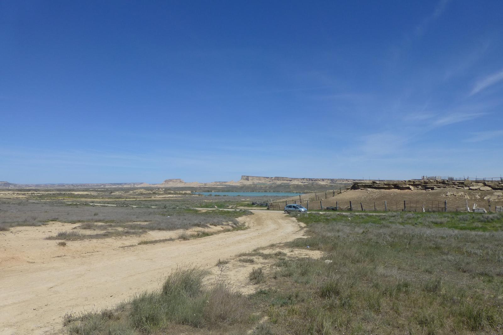 Pista de tierra con un vehículo circulando, típica del recorrido en coche por la Bardena Blanca