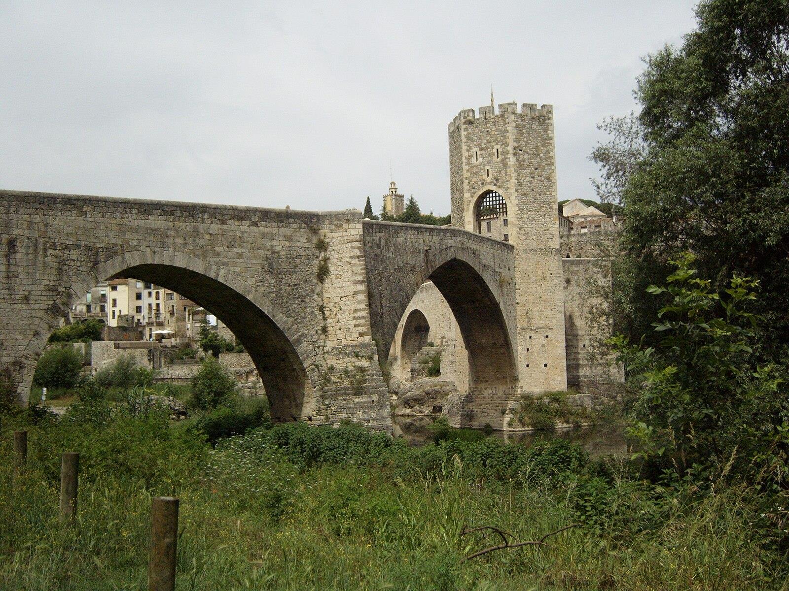 Vista general del puente medieval de Besalú con sus arcos sobre el río Fluvià y vegetación en la ribera