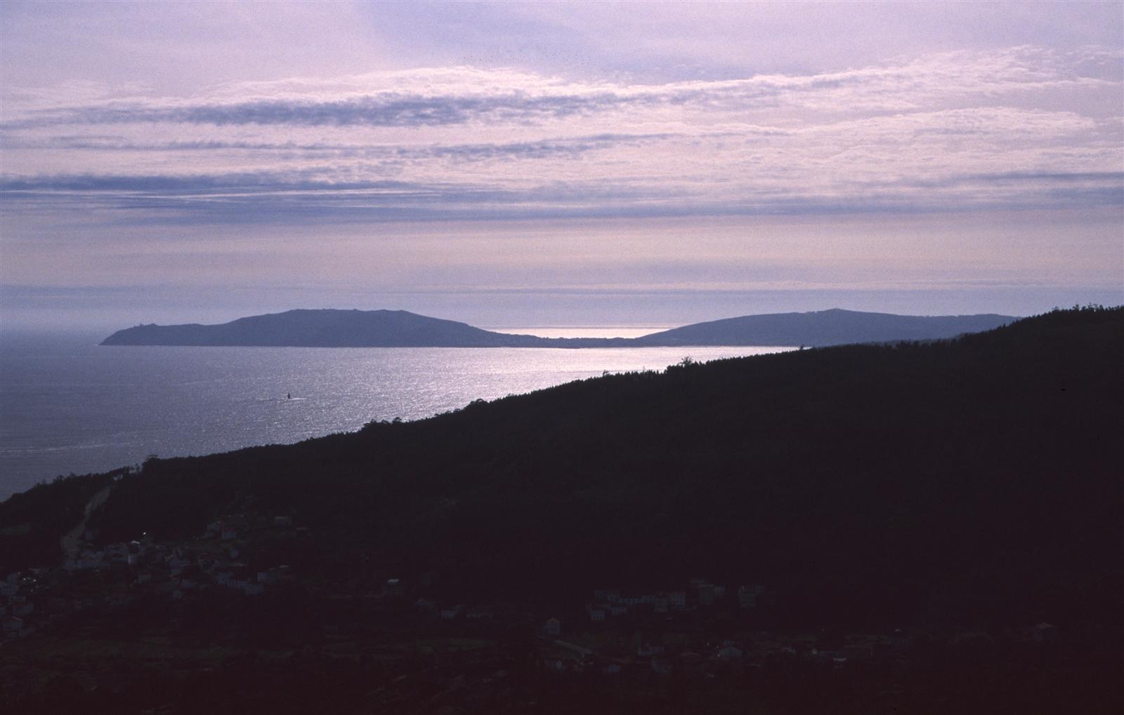 Vista del cabo y el faro de Fisterra desde el mar, con los acantilados y el promontorio granítico, A Coruña, Galicia
