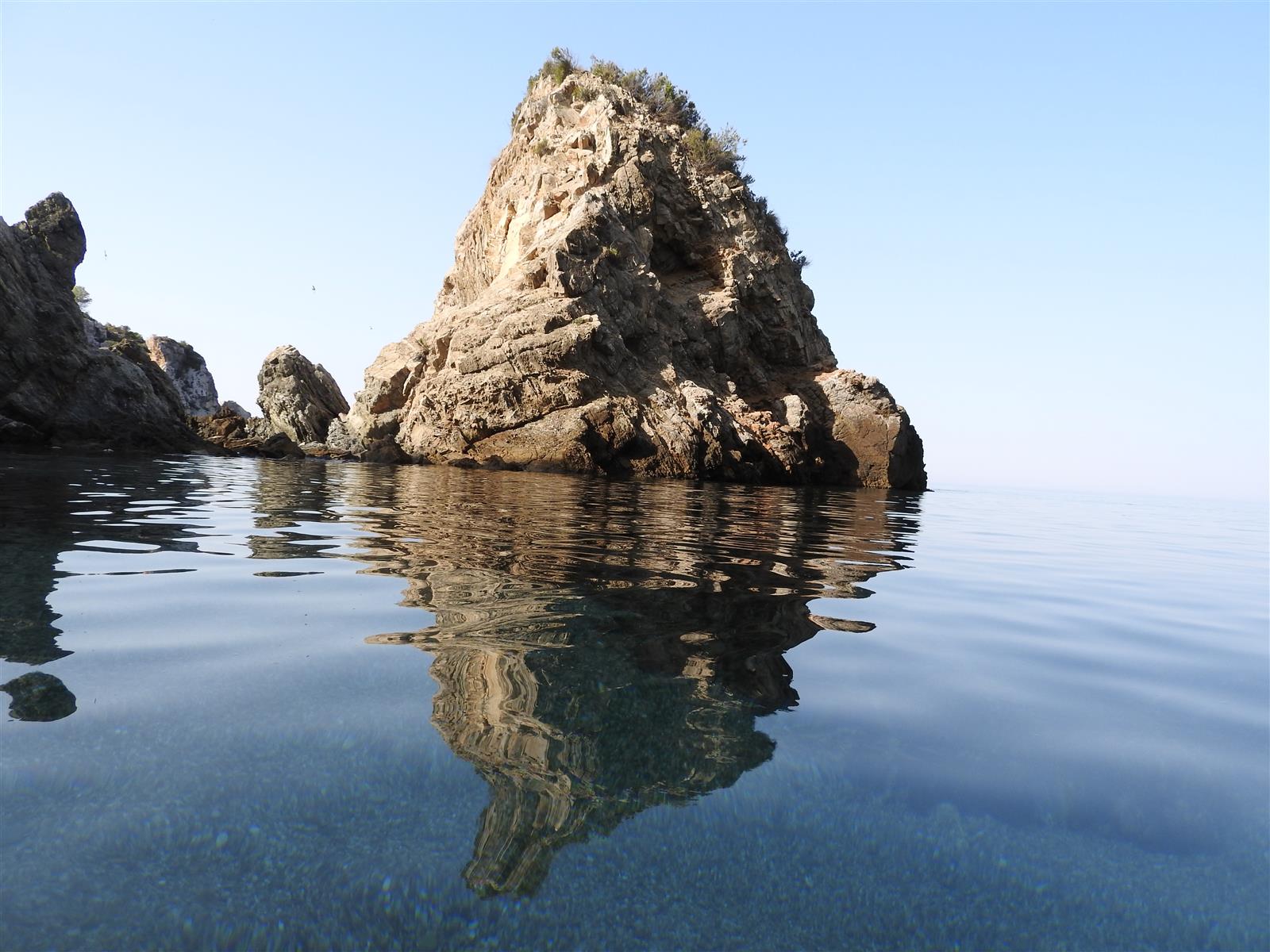 Peñón del Fraile reflejado en el agua cristalina de Cala del Cañuelo en Maro, Nerja