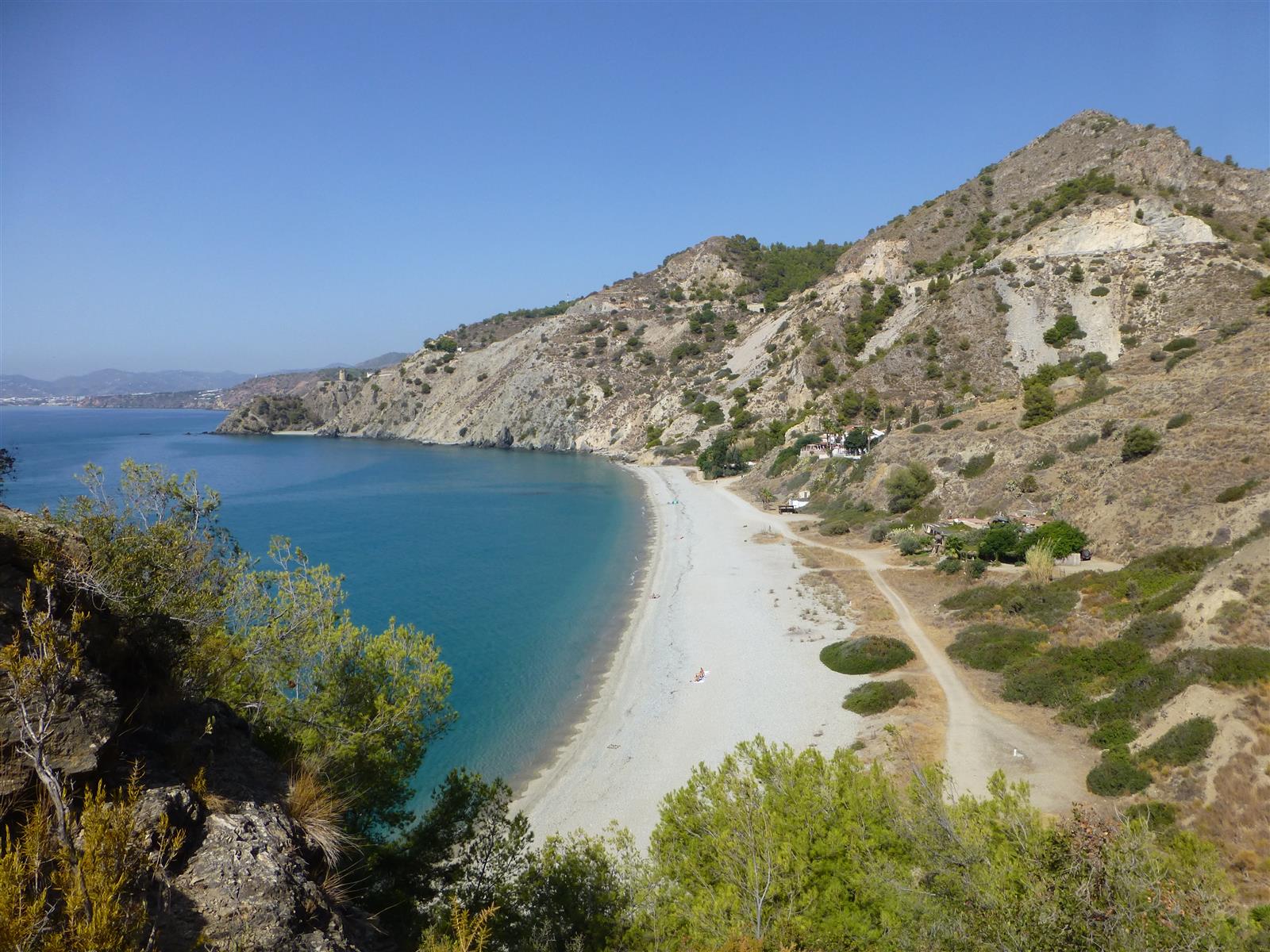 Vista panorámica desde altura de Cala del Cañuelo con playa de cantos, agua turquesa y acantilados en Nerja