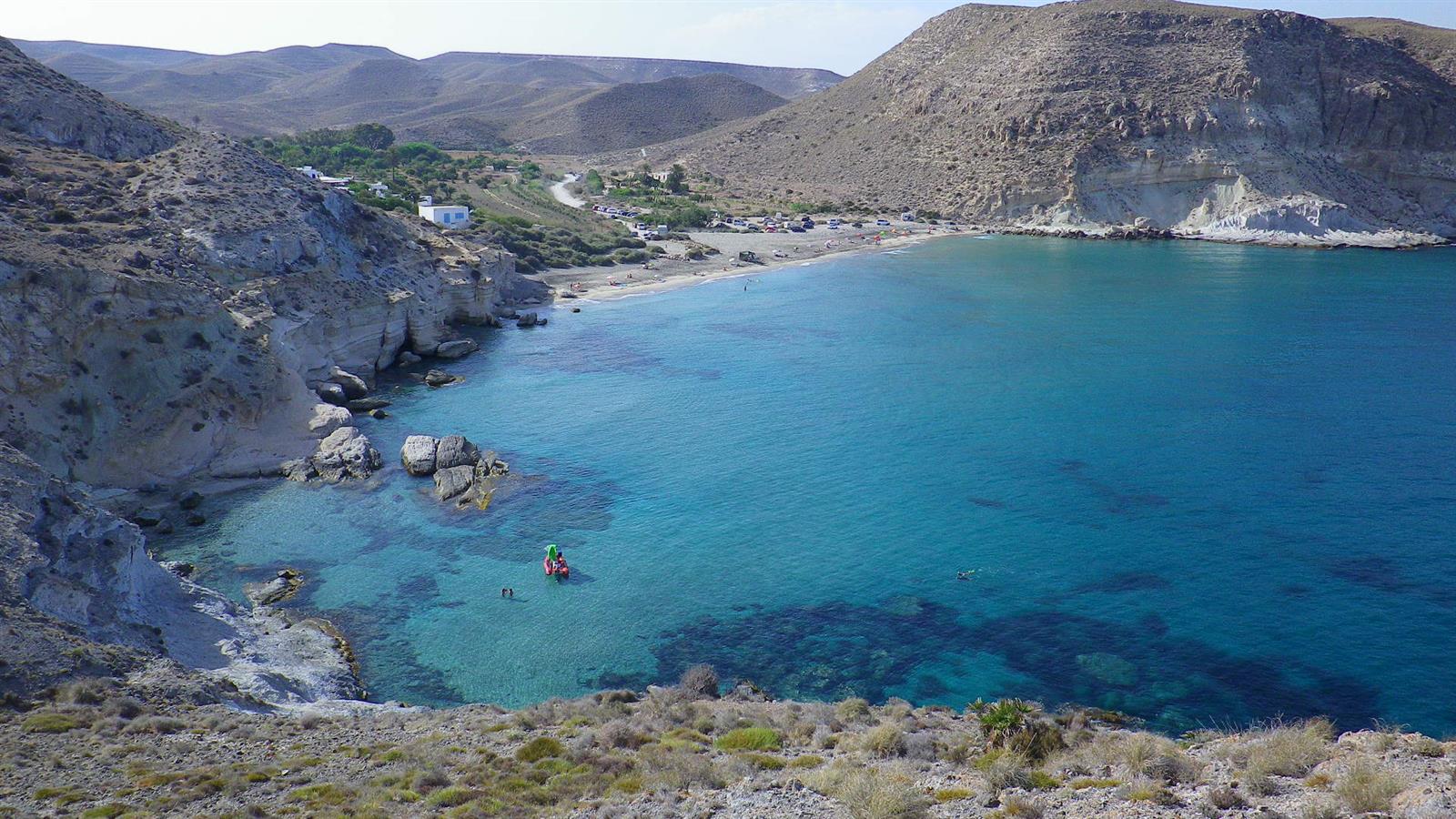 Vista panorámica de Cala del Plomo desde la ladera con bahía turquesa, acantilados de calcarenita y montañas áridas del Cabo de Gata