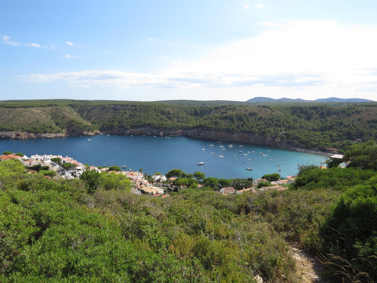 Vista desde mirador de Cala Montgó con la bahía protegida, barcos, pinos y la forma reconocible de la cala en L'Escala, Girona