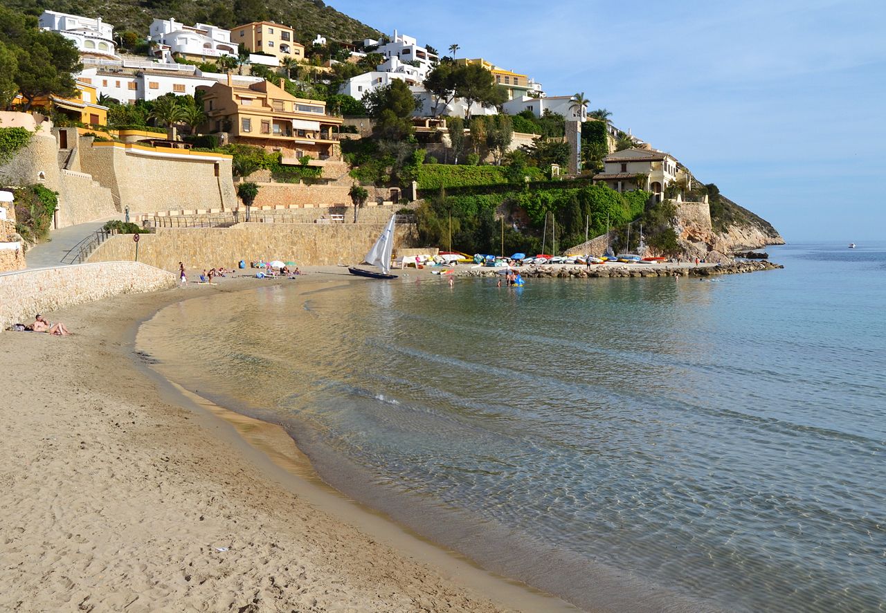 Vista de la playa del Portet de Moraira con casas blancas y agua tranquila, Alicante