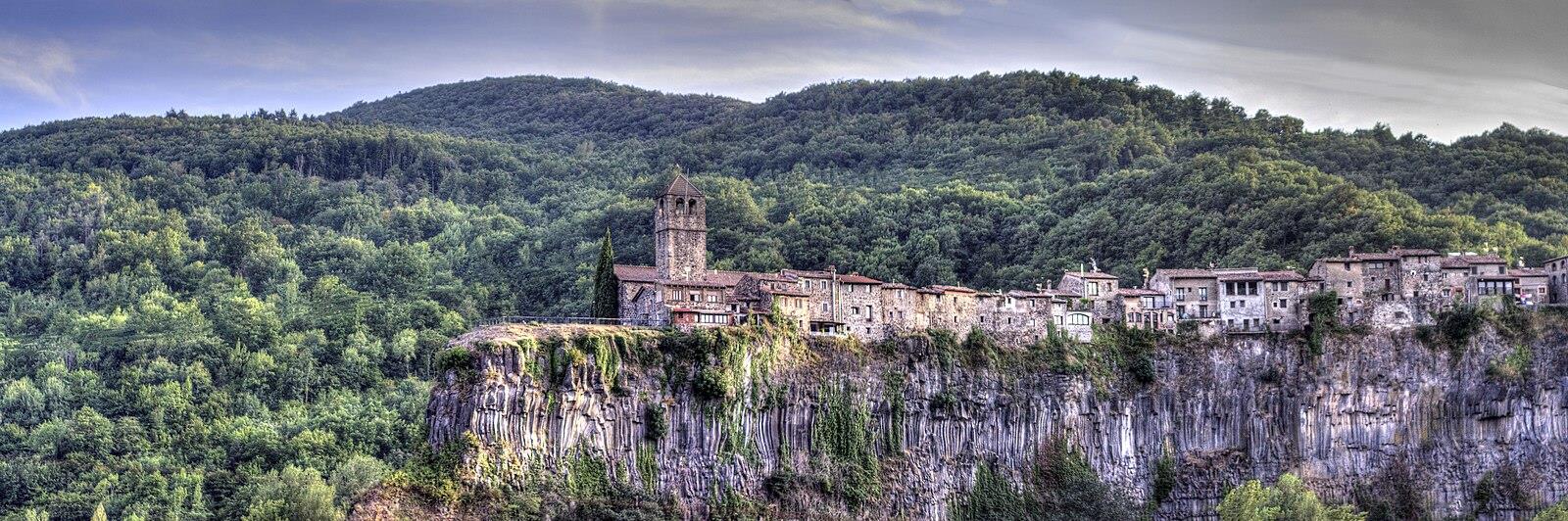 Panorámica amplia de Castellfollit de la Roca sobre el risco basáltico de la Garrotxa, con el bosque y las colinas volcánicas al fondo