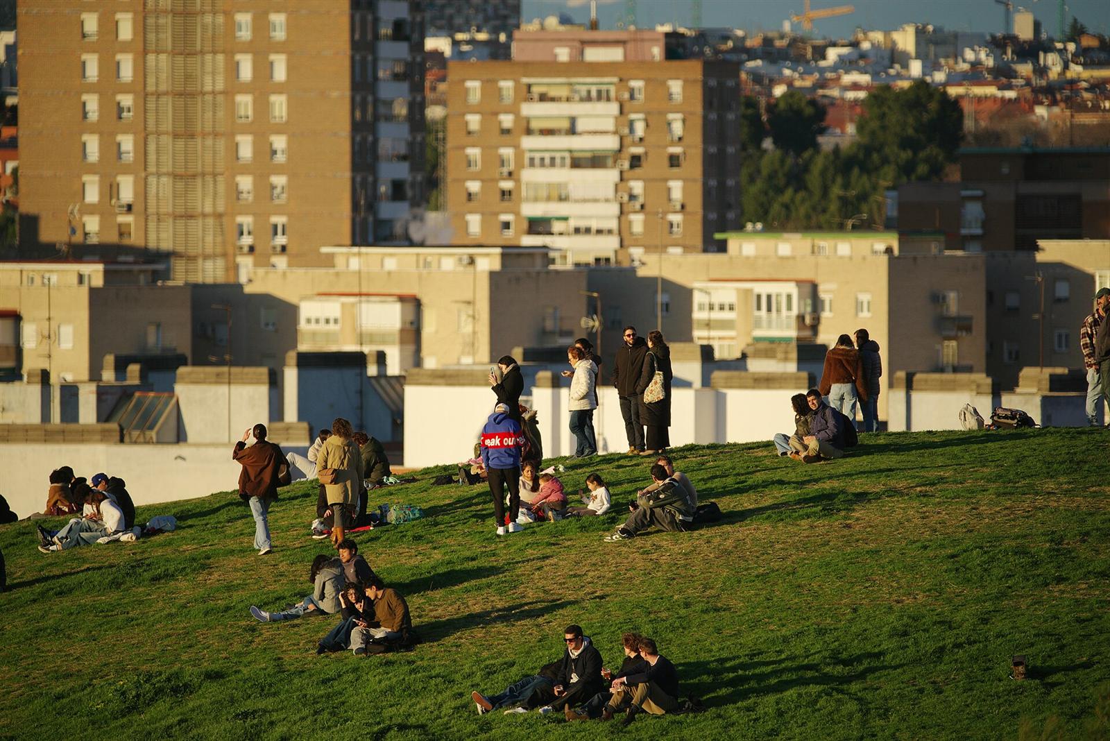 Gente disfrutando del atardecer sobre el césped, con el skyline de Madrid al fondo