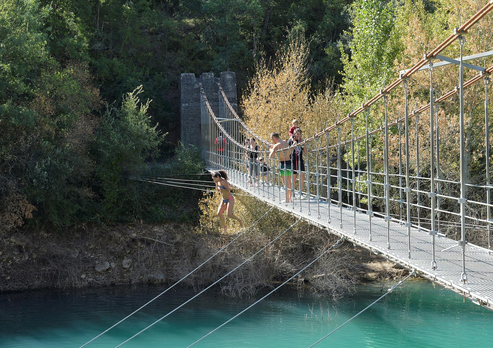 Puente colgante del congost con visitantes bañándose en el río