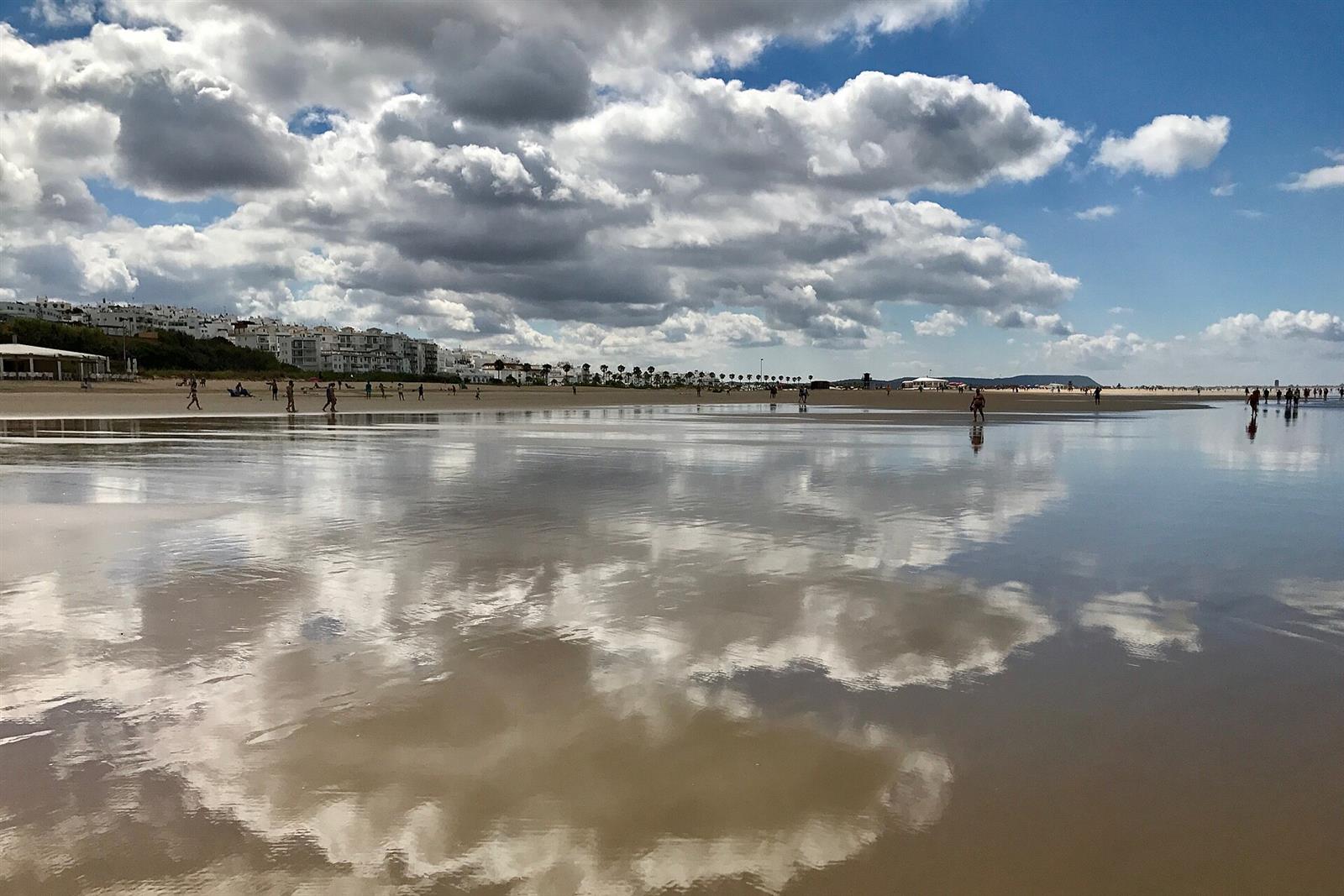 Playa de los Bateles de Conil de la Frontera con reflejo de nubes y el pueblo blanco al fondo, Cádiz