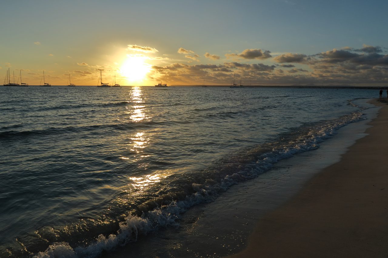 Playa de Es Trencs al atardecer, con los colores dorados del sol reflejados en el agua