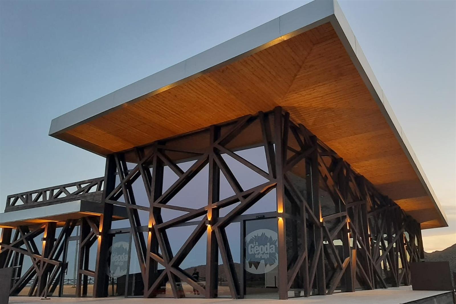 Centro de visitantes de la Geoda de Pulpí al atardecer, edificio de arquitectura moderna con estructura metálica y madera, con el rótulo de La Geoda de Pulpí visible