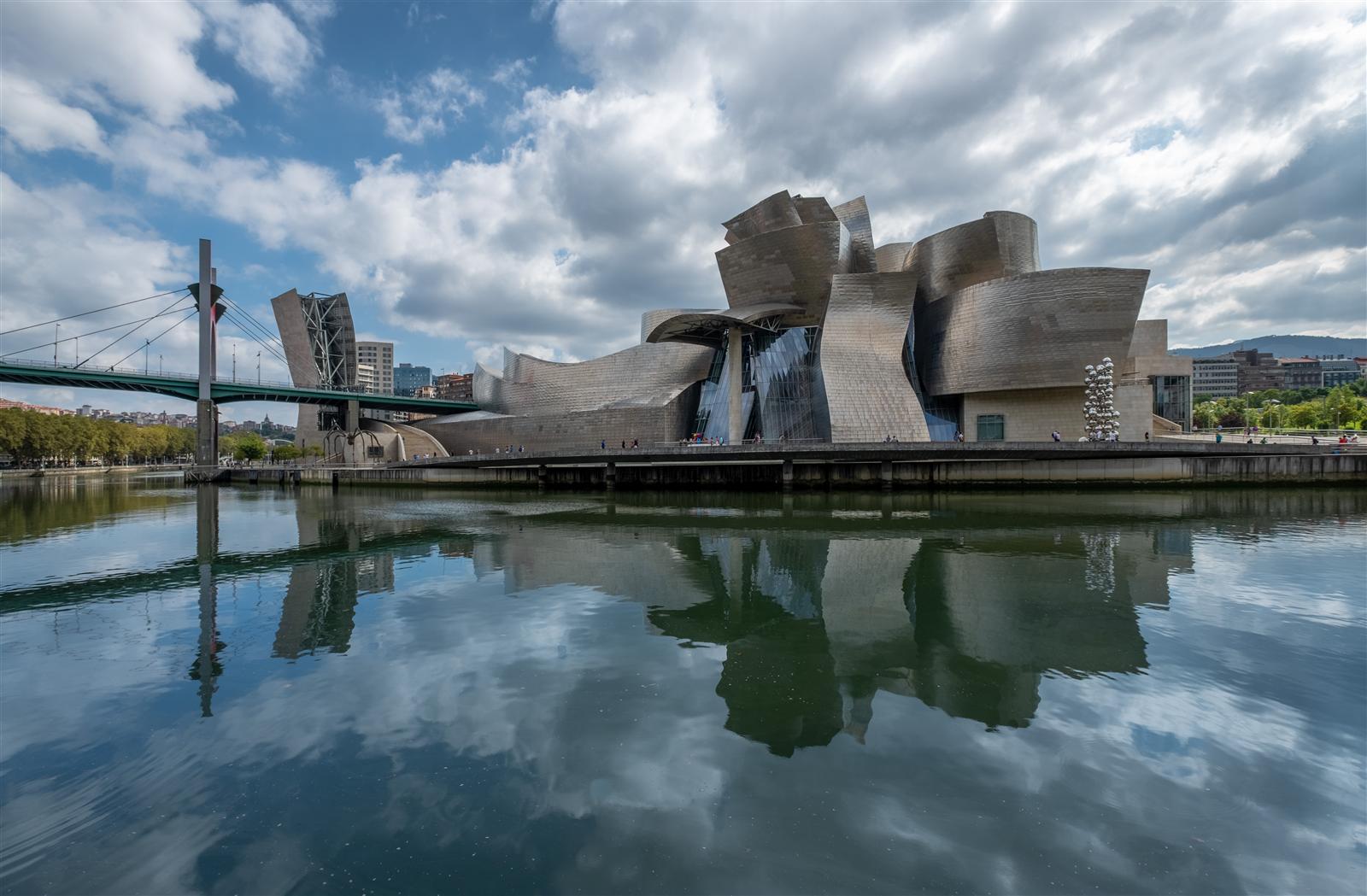 Vista gran angular del Guggenheim Bilbao desde la orilla opuesta del Nervión, con el Puente de La Salve al fondo y el complejo museístico completo, Bilbao