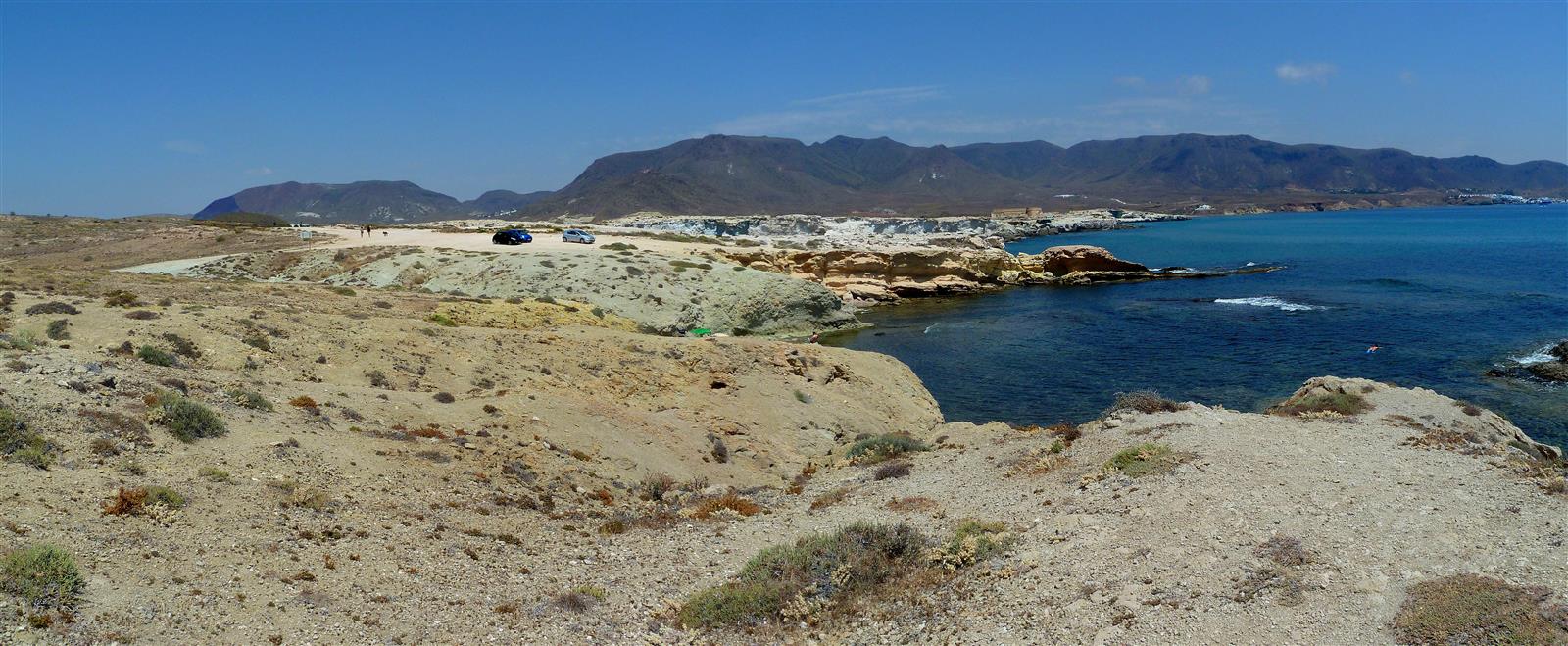 Vista costera panorámica de Los Escullos con formaciones volcánicas en primer plano, agua turquesa y la línea de montañas áridas al fondo