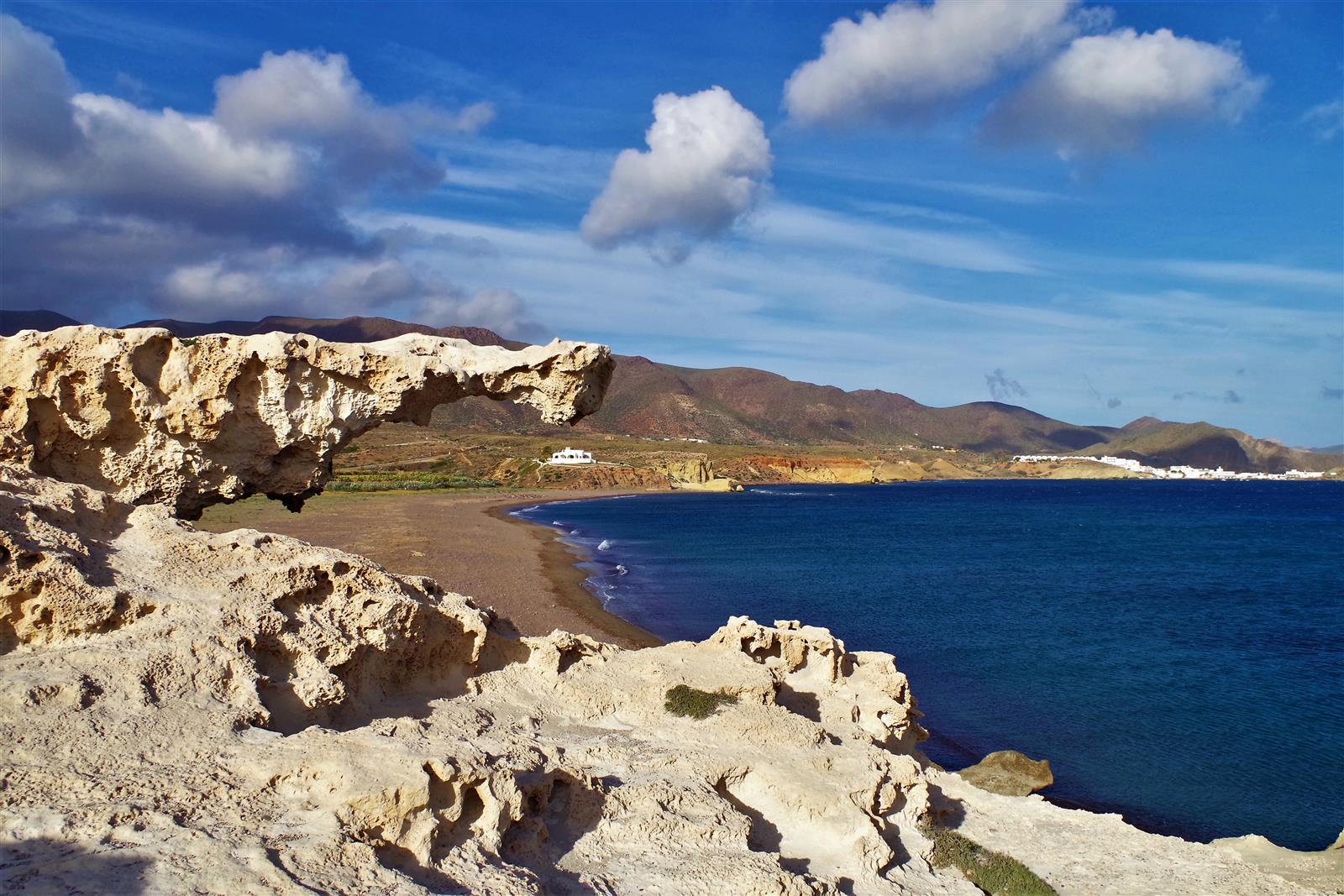 Arco de la duna fósil de calcarenita de Los Escullos visto desde el exterior, con la playa y el mar azul intenso al fondo bajo cielo con nubes