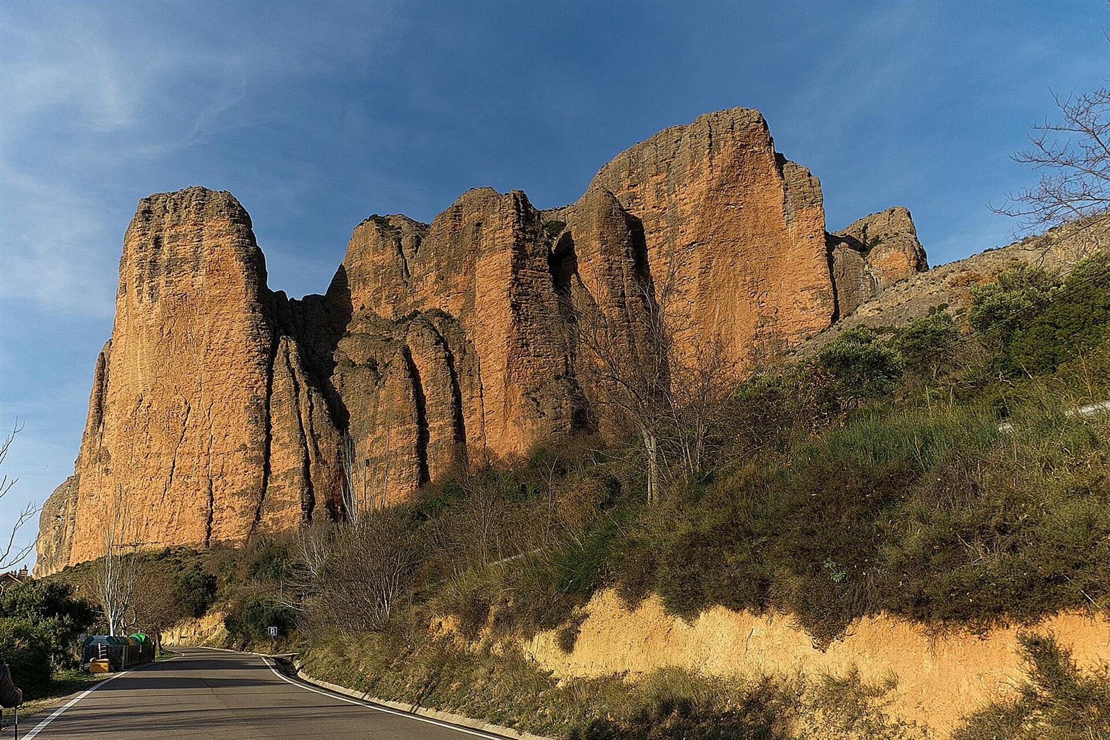 La pared de los mallos iluminada al atardecer, con la carretera al pie para dar escala