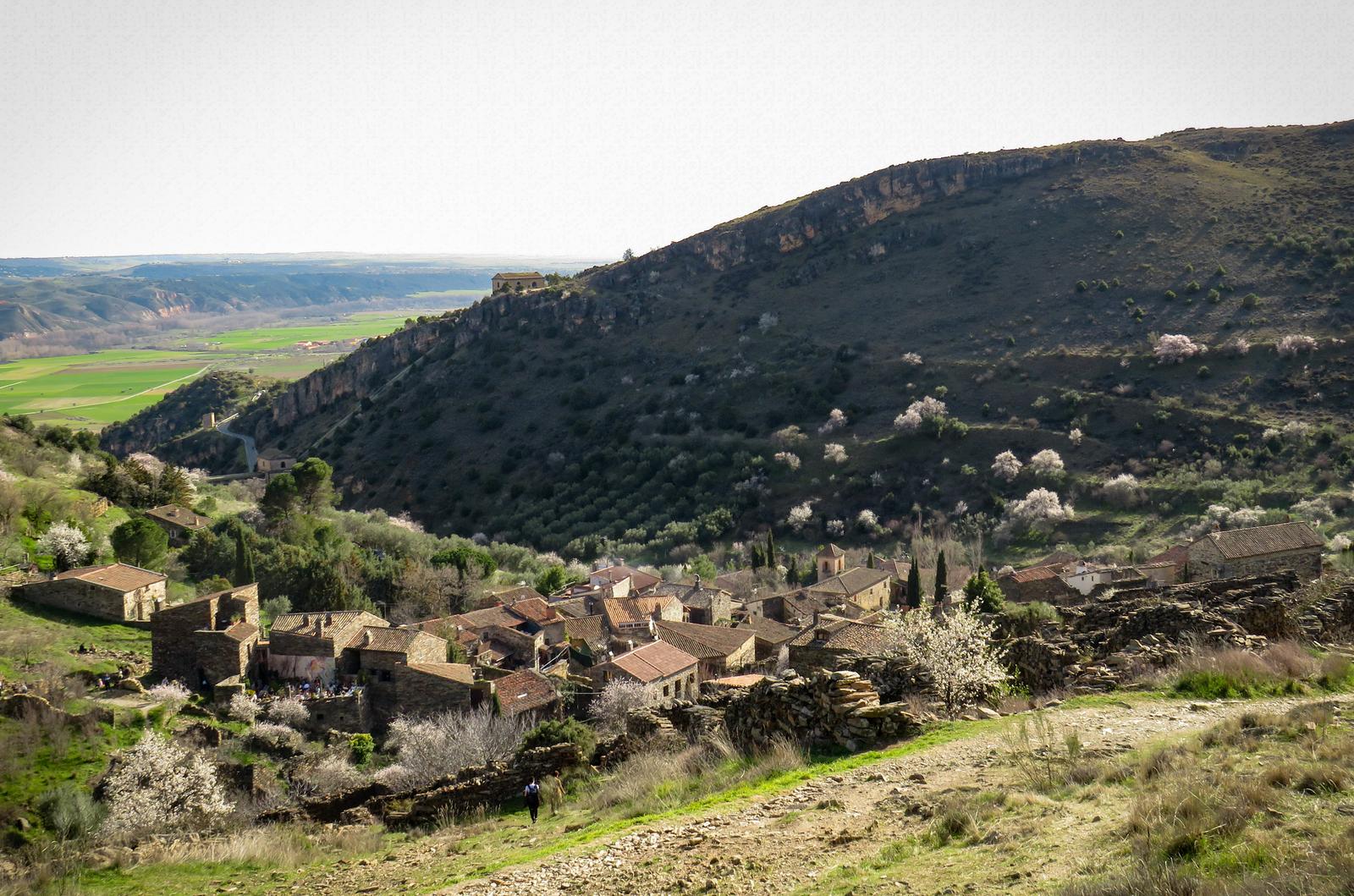 Senderistas acercándose al pueblo por el camino de acceso, con el valle al fondo
