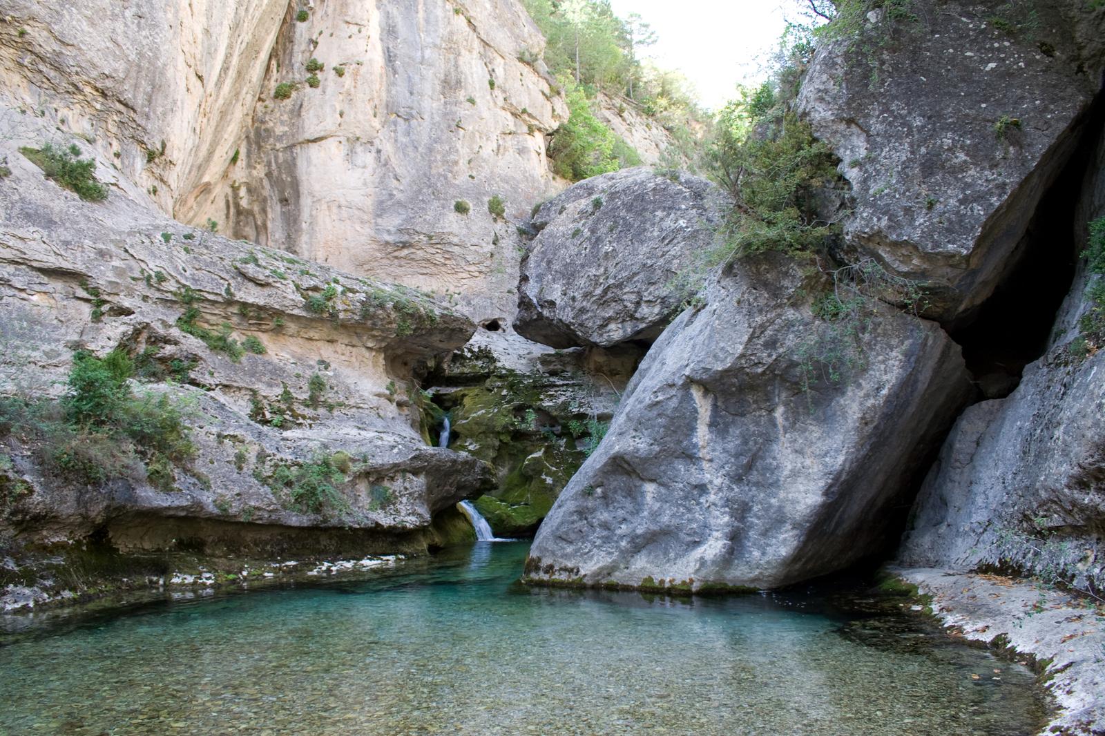 Poza de agua turquesa en el nacimiento del río Pitarque, entre paredes de roca caliza