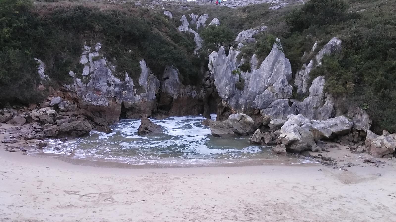 Vista de la cala desde el acceso, con formaciones de roca caliza y oleaje entrando por el canal