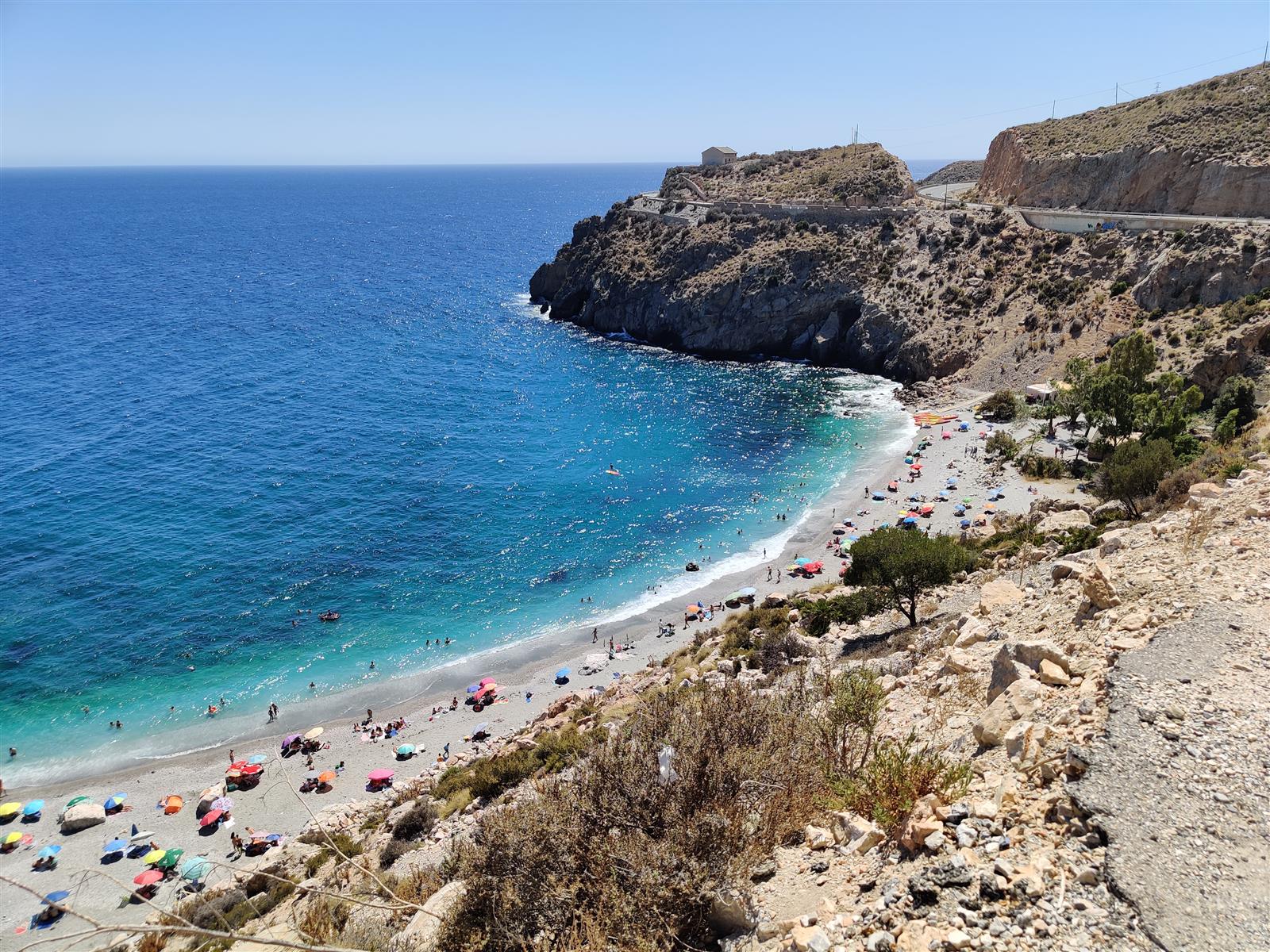 Playa de La Rijana desde el acantilado derecho, con el canto rodado de la orilla, el agua turquesa y el acantilado rocoso al fondo