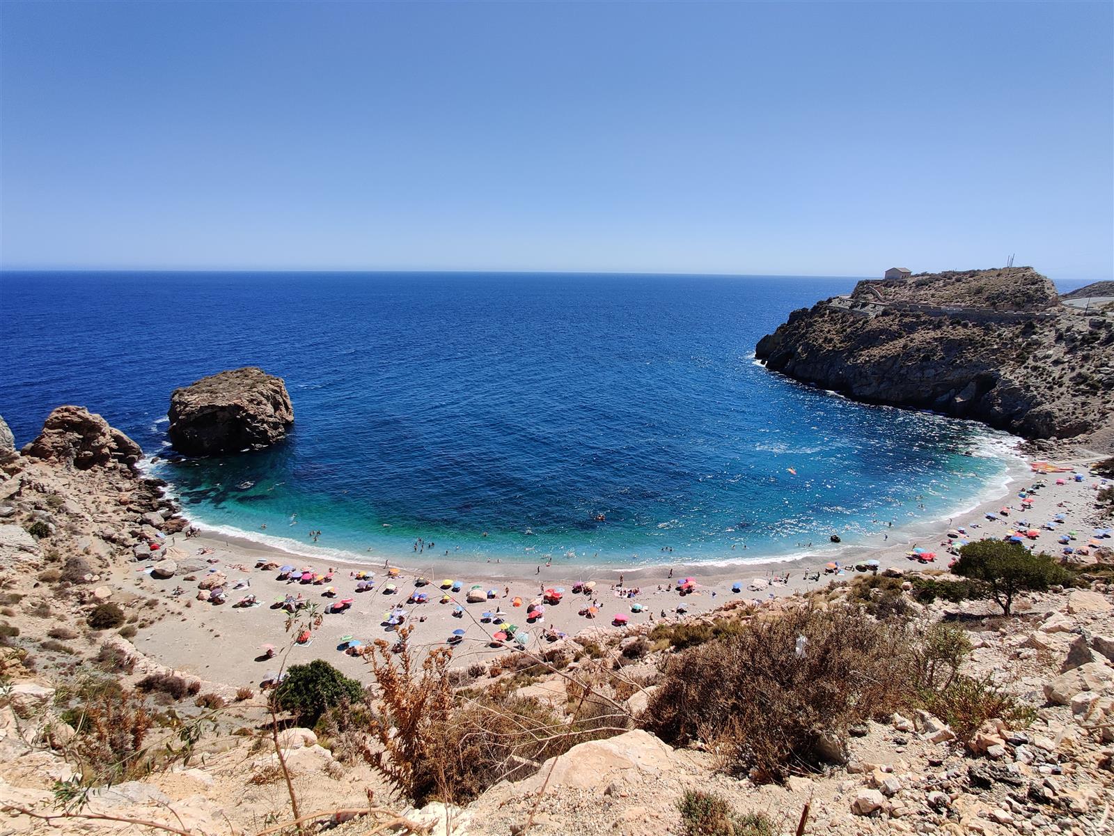 Panorámica de la Playa de La Rijana desde el acantilado, con la cala en herradura, agua azul-turquesa y sombrillas en verano, en Gualchos, Granada
