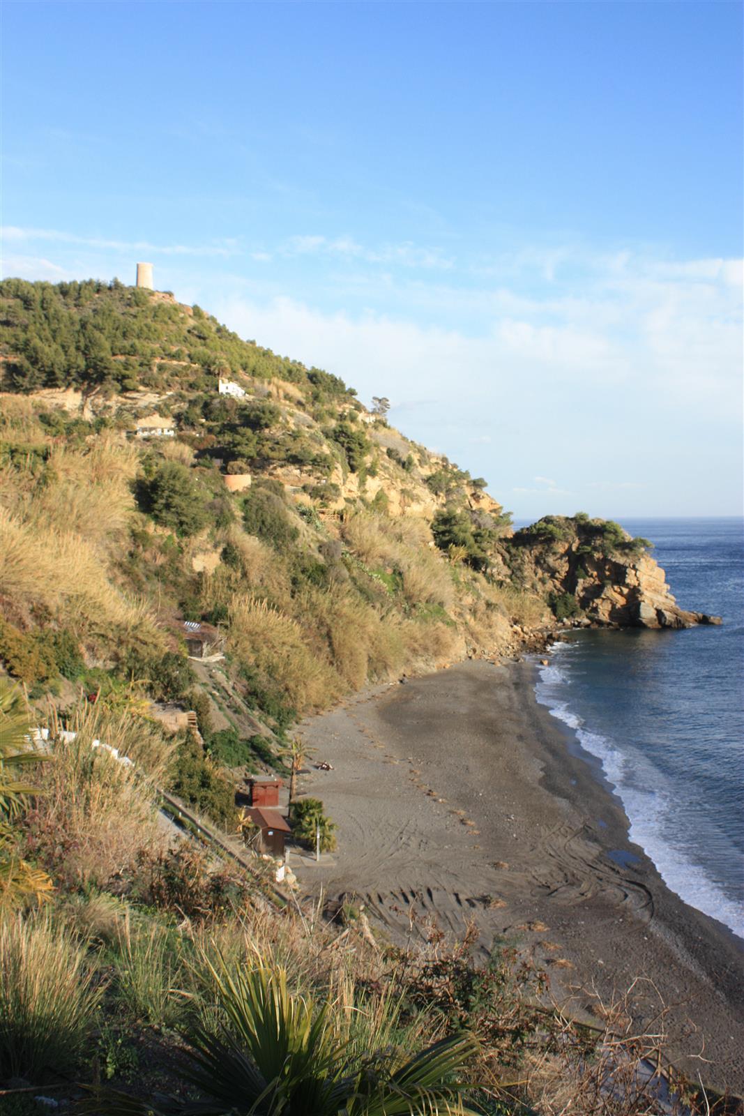Vista panorámica vertical de la Playa de Maro desde el acantilado con promontorio rocoso y mar mediterráneo