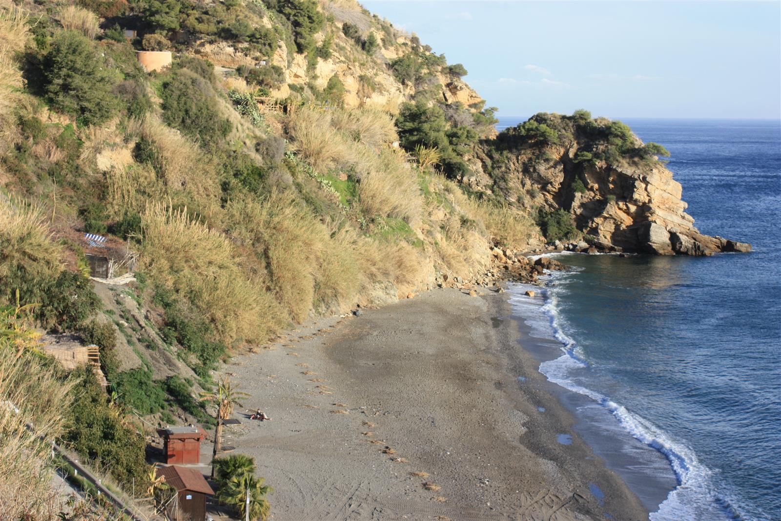 Vista aérea de la Playa de Maro desde el acantilado, con playa de arena y canto, mar azul y ladera mediterránea en Nerja