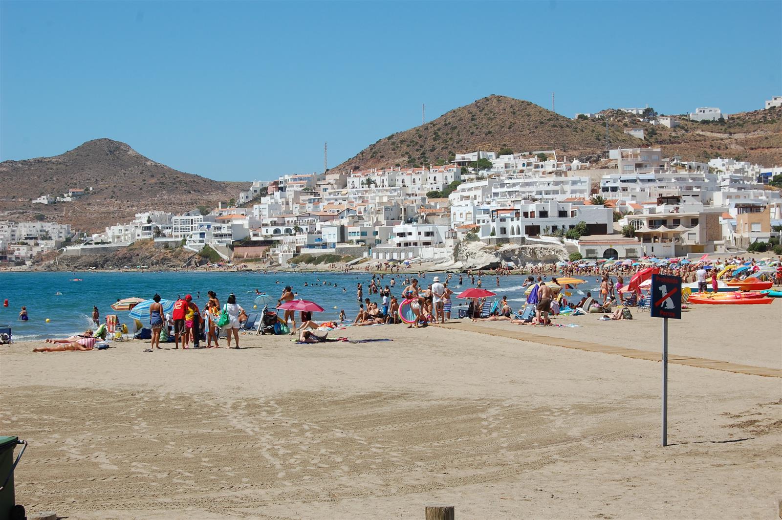 Playa de San José llena de bañistas en verano con el pueblo blanco y las montañas volcánicas de Cabo de Gata al fondo