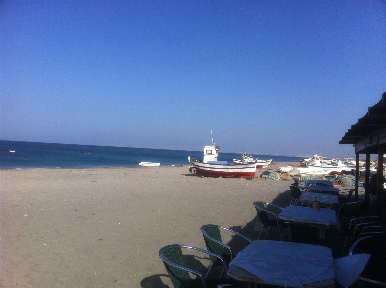 Barcas de pesca varadas en la arena de San José con una terraza de chiringuito en primer plano y el mar al fondo