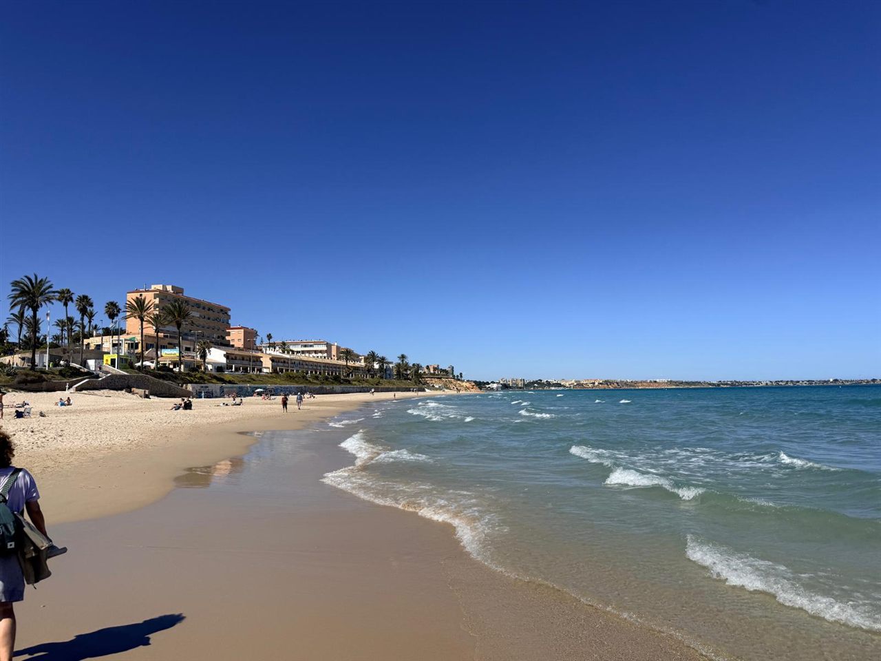 Orilla de la Playa de Mil Palmeras con las olas del Mediterráneo y el complejo hotelero al fondo