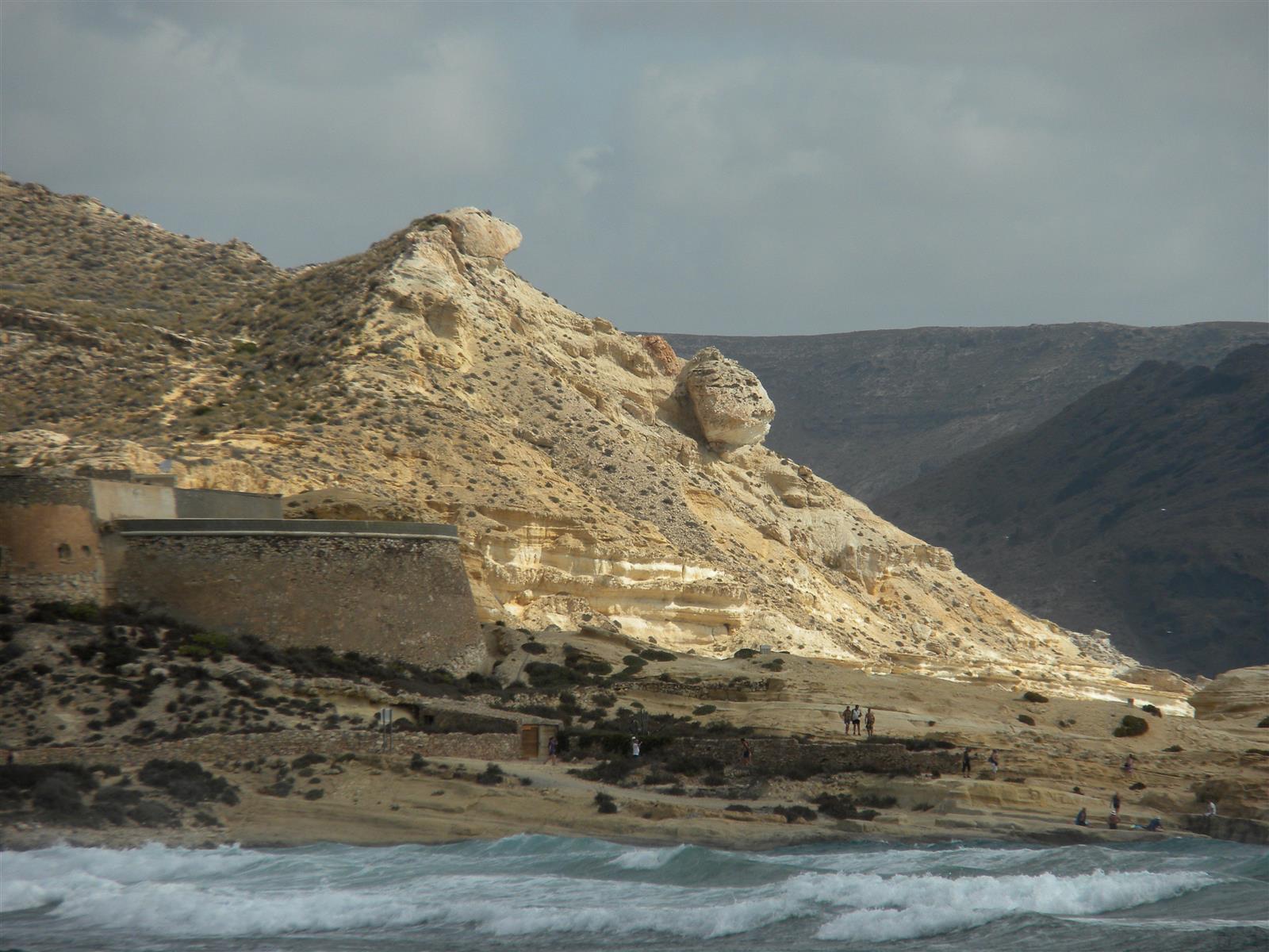 Detalle del Castillo de San Ramón sobre la roca volcánica de El Playazo, con el mar al pie y bañistas en la orilla