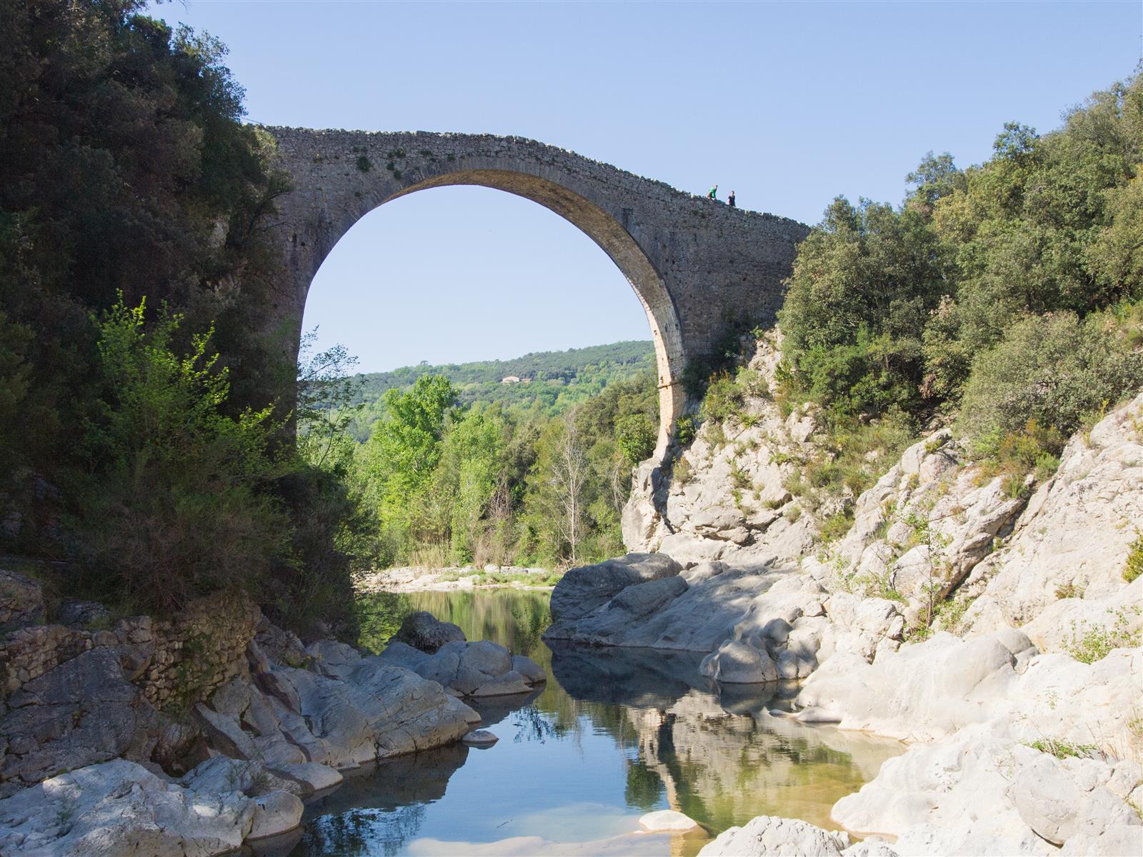 Pont de Llierca en primavera: el arco de piedra con agua verde bajo el puente y vegetación en las orillas del río Llierca