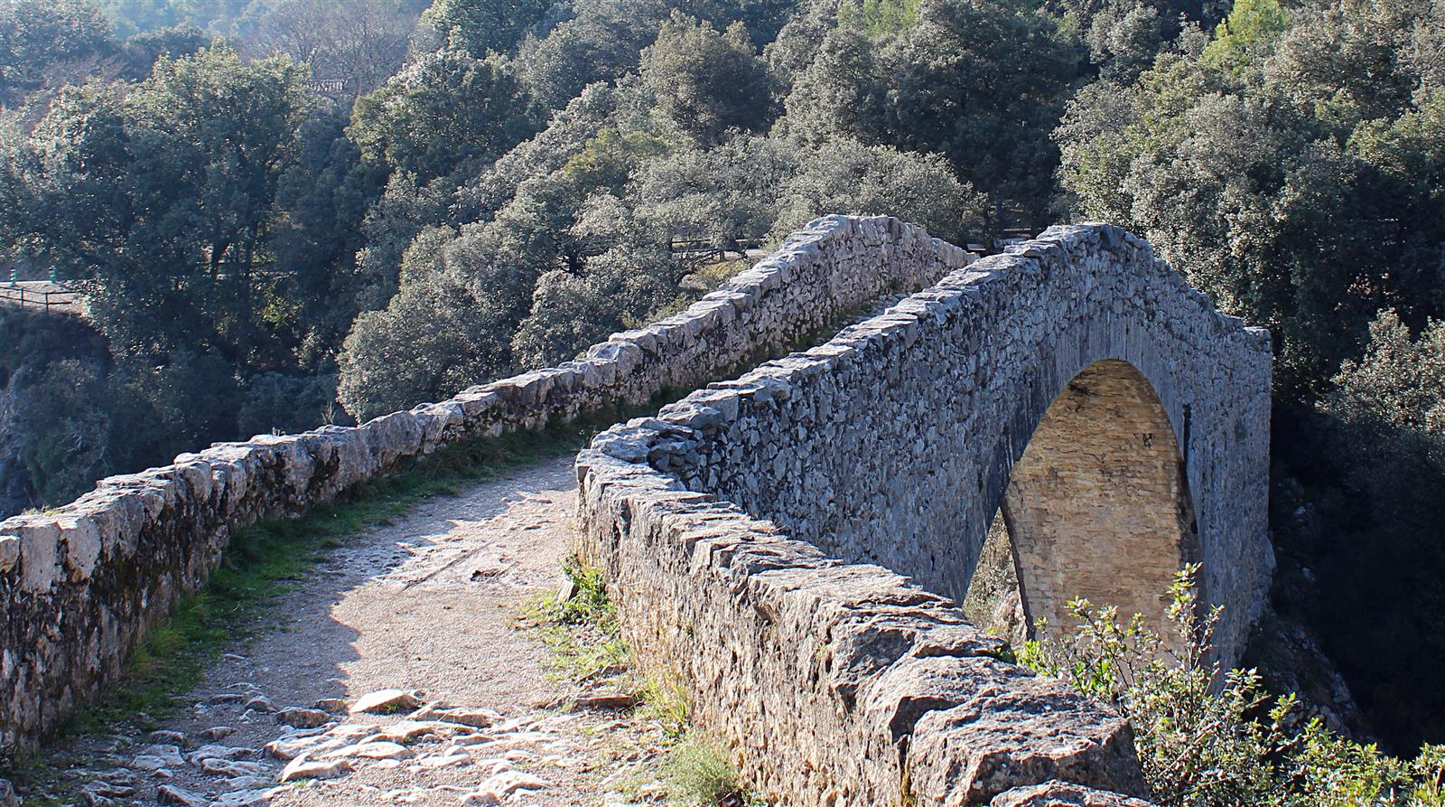 Perspectiva desde la parte superior del Pont de Llierca: el camino de tierra que atraviesa el puente con el arco de piedra visible y el entorno natural del río Llierca