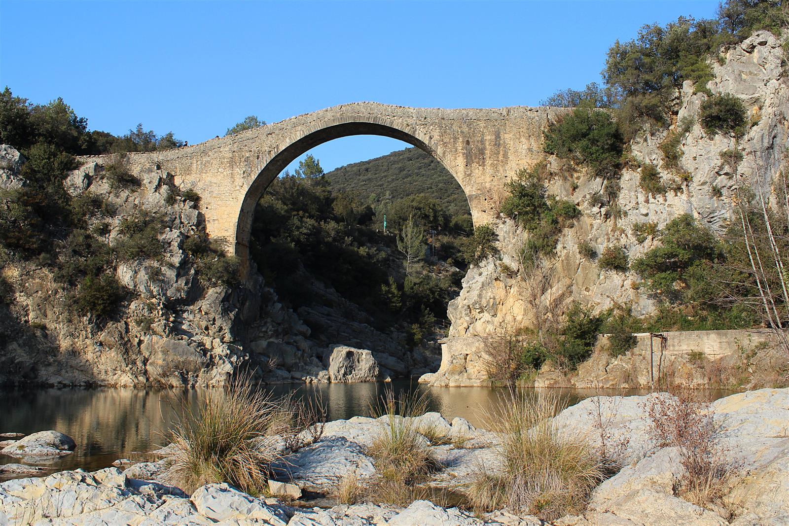 Pont de Llierca: arco de piedra medieval sobre el río Llierca con pozas de agua y rocas blancas bajo el arco, La Garrotxa, Girona
