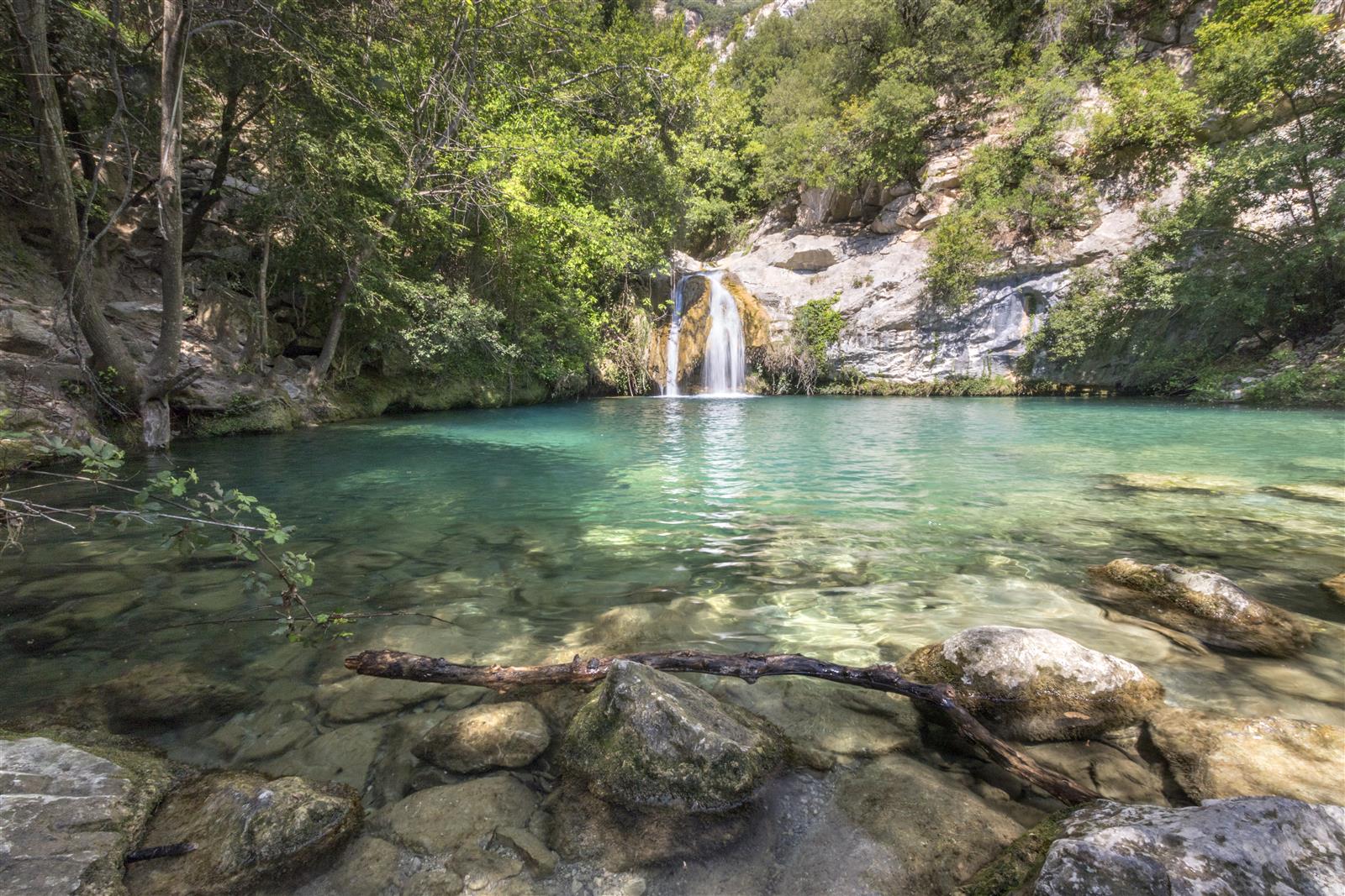 Gorga Fosca de Sadernes: poza de agua turquesa entre rocas y árboles en el cauce del río Sant Aniol, con una cascada cayendo desde la roca
