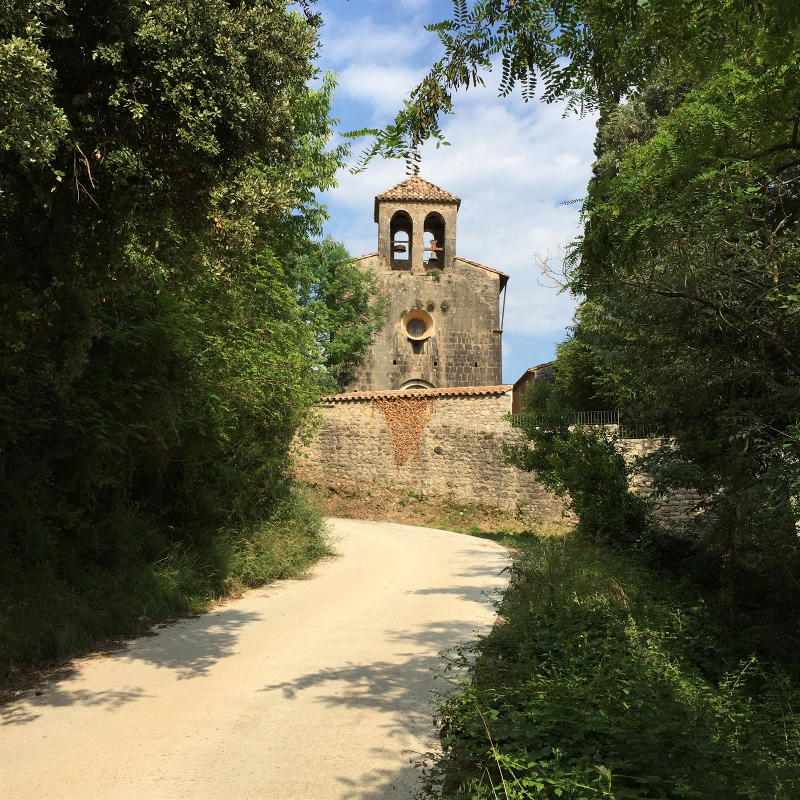La ermita y el campanario del núcleo de Sadernes entre árboles y vegetación mediterránea, la pequeña aldea de la Alta Garrotxa