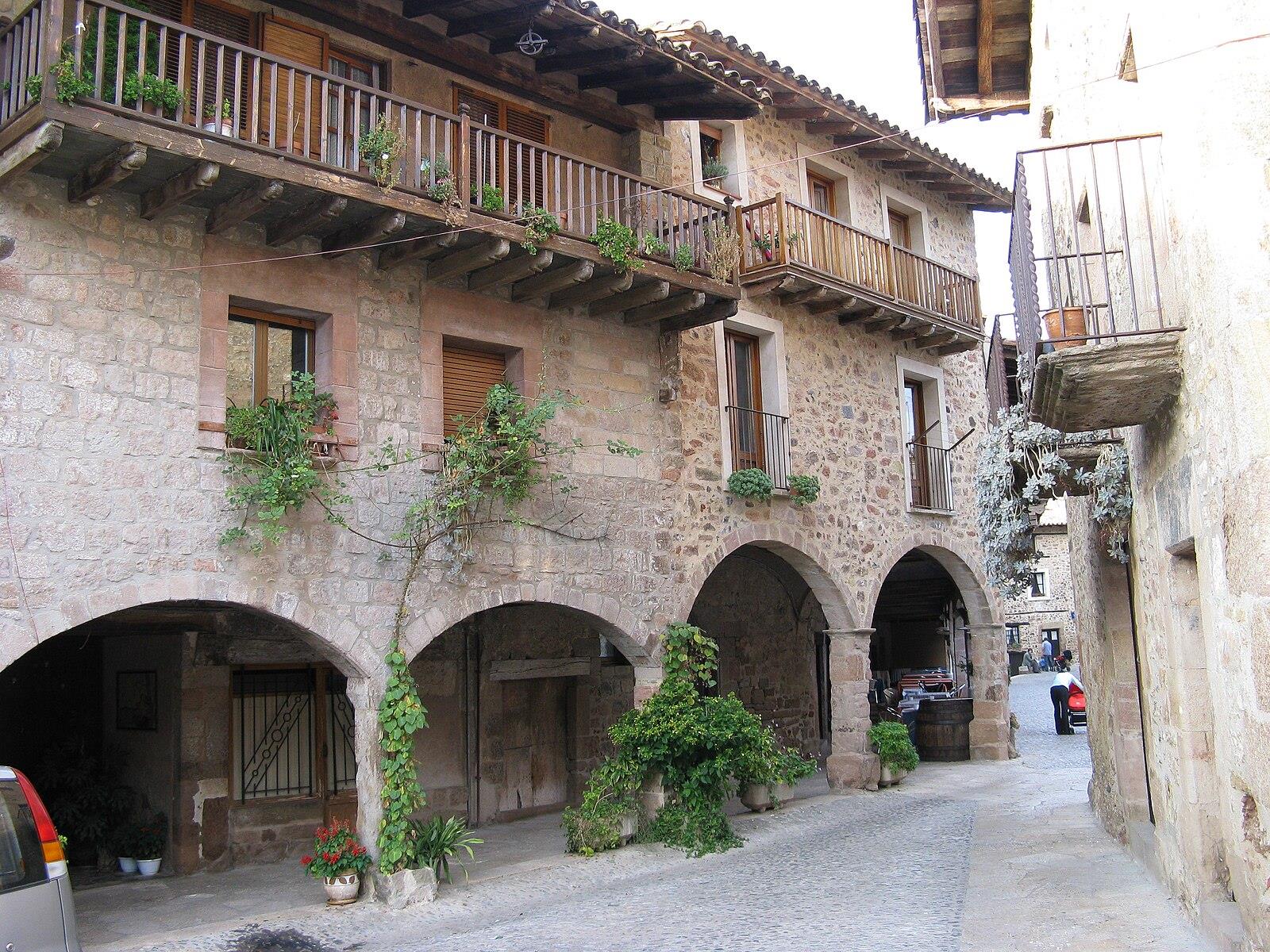 Calle porticada con arcos de piedra, balcones con plantas y adoquines en el casco histórico de Santa Pau, La Garrotxa