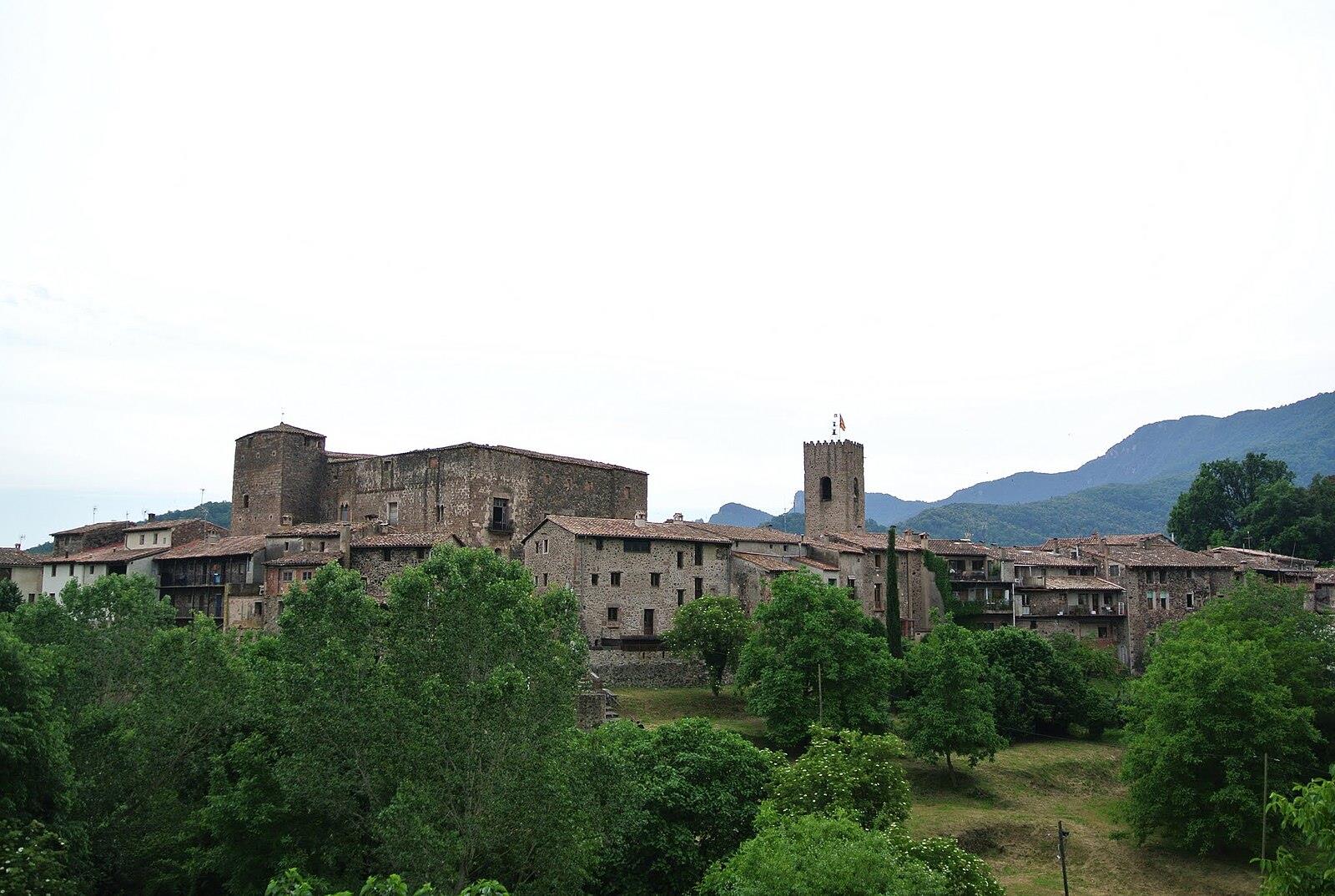 Panorámica de Santa Pau con el castillo y la torre de la iglesia visibles sobre el conjunto medieval rodeado de vegetación en La Garrotxa