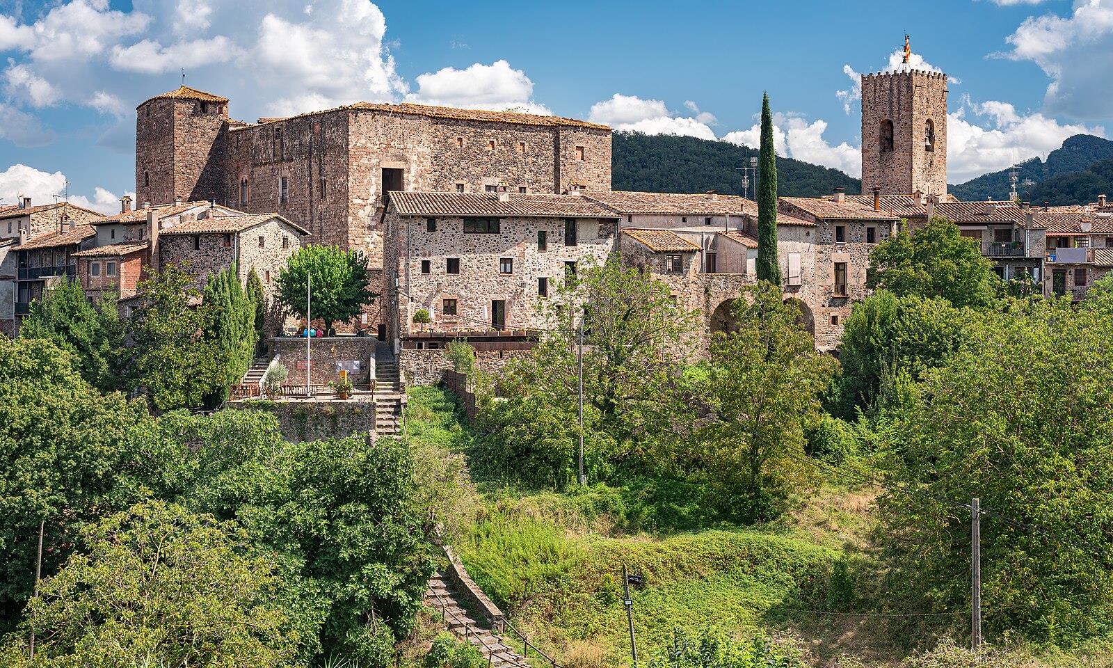 Vista exterior de Santa Pau con el castillo medieval, la torre campanario y las casas de piedra rodeadas de vegetación, La Garrotxa, Girona