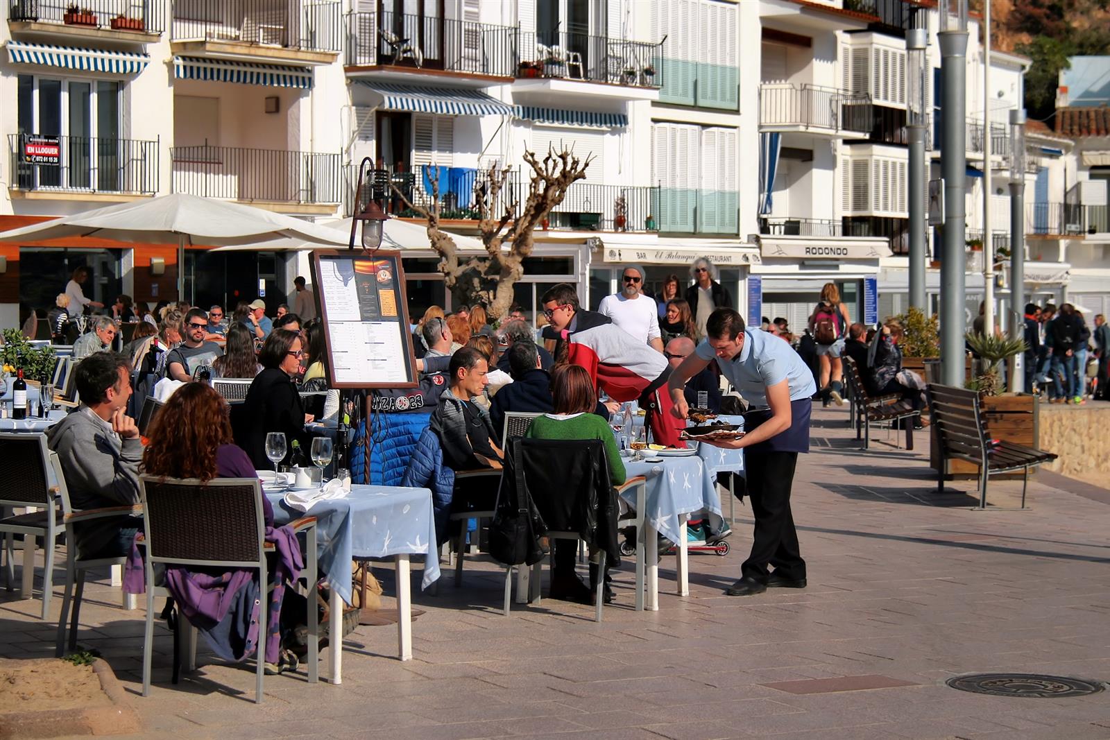 Terraza de restaurante en el paseo marítimo de Tamariu con ambiente marinero y casas blancas al fondo, Palafrugell