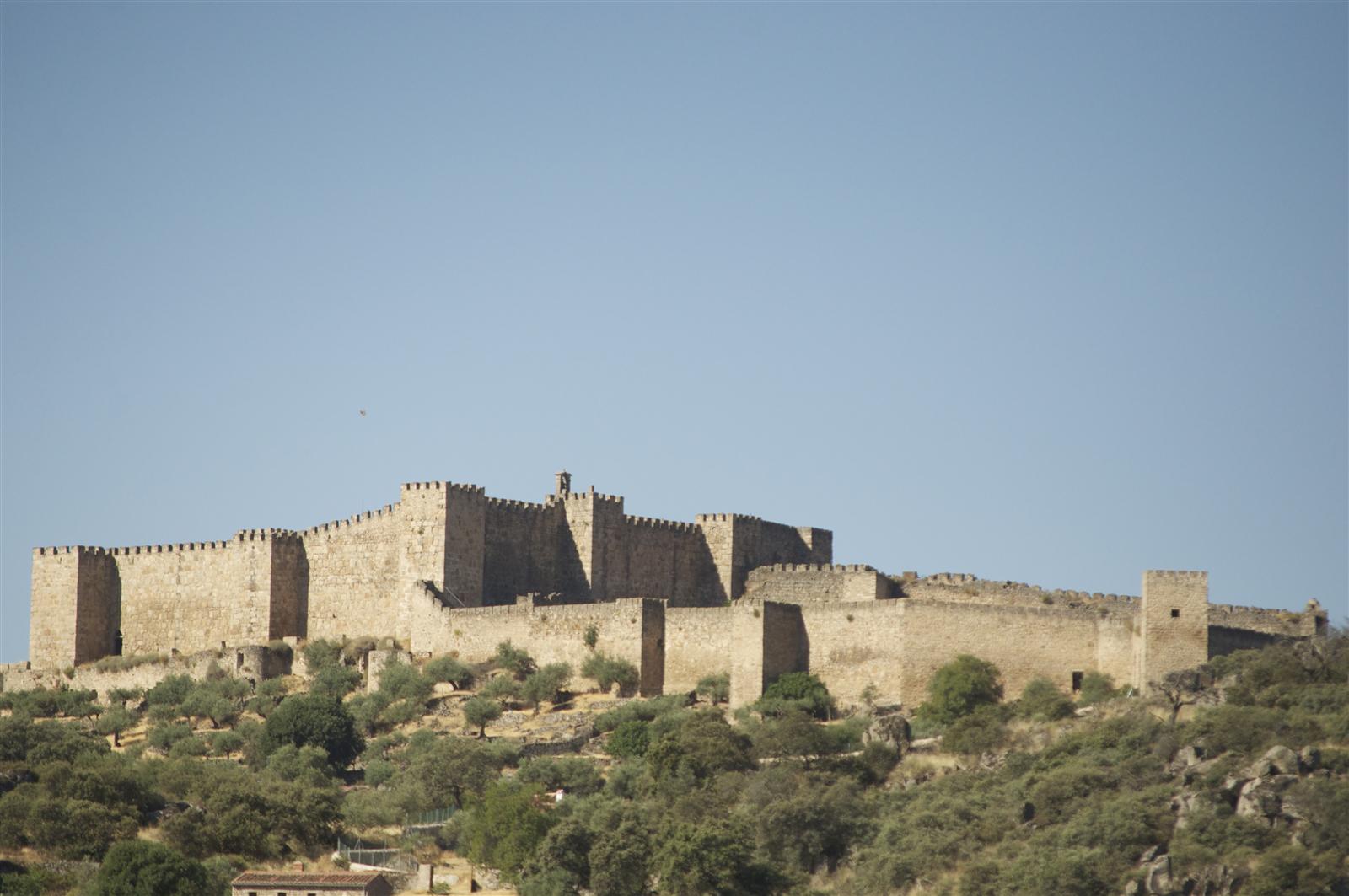 Castillo de Trujillo visto desde la ladera del cerro granítico, con la muralla almenada, las torres y el cielo azul de Extremadura al fondo