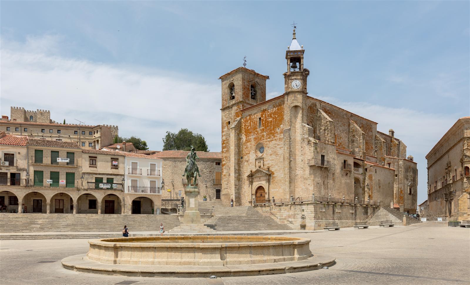 Plaza Mayor de Trujillo (Cáceres) con la estatua ecuestre de Francisco Pizarro en primer plano y la iglesia de San Martín con sus torres al fondo, bajo cielo azul intenso de Extremadura