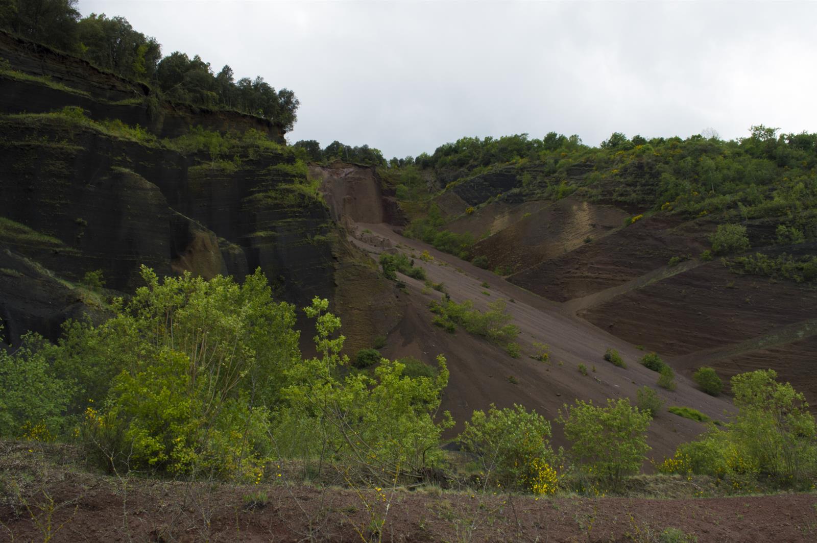 Gredera del Volcán Croscat: corte volcánico con capas de ceniza rojiza y tierra oscura en el Parc Natural de la Zona Volcànica de La Garrotxa, Girona