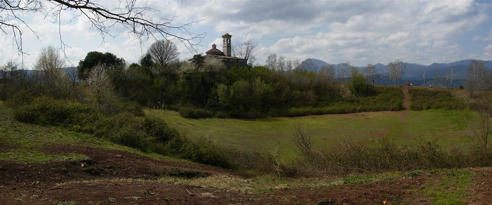 Panorámica del cráter del Volcán Montsacopa desde el interior: cuenco volcánico verde con la ermita de Sant Francesc y las montañas de La Garrotxa al fondo