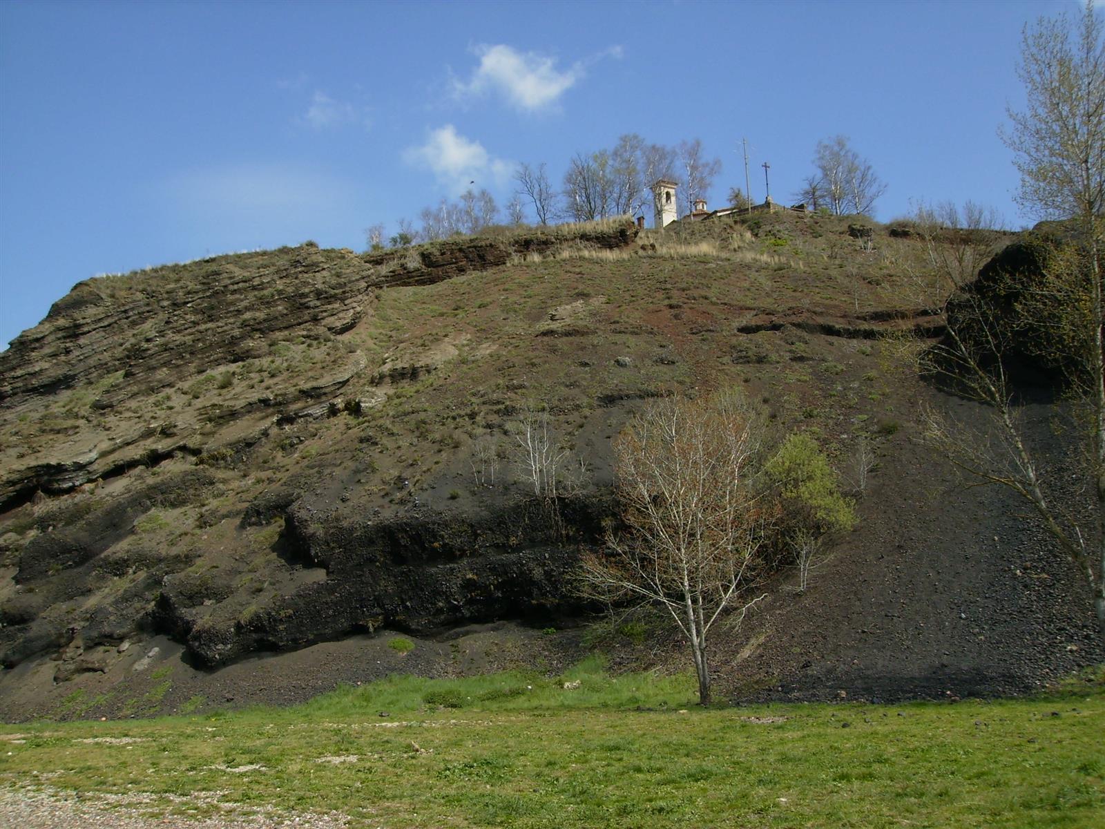 Gredera del Volcán Montsacopa: corte volcánico con capas de basalto oscuro y la iglesia de Sant Francesc en la cima, Olot, La Garrotxa